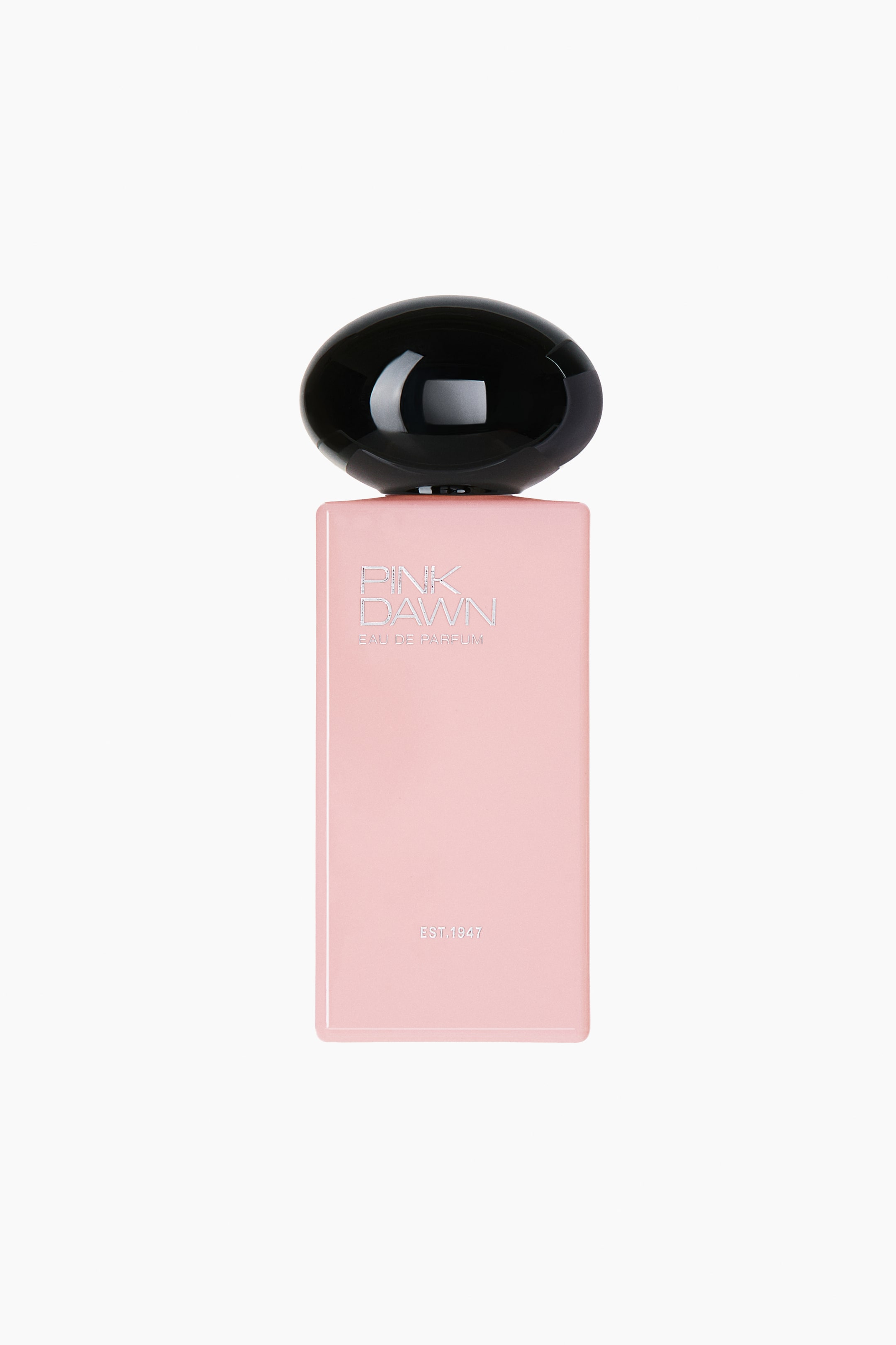 Agrandir l'image: L’Eau de Parfum Pink Dawn est présentée de face, dans un flacon rectangulaire rose mat surmonté d’un grand bouchon noir brillant aux formes arrondies. Une inscription argentée sur la partie supérieure du flacon affiche « PINK DAWN EAU DE PARFUM », tandis que la mention « EST. 1947 » apparaît près du bas.