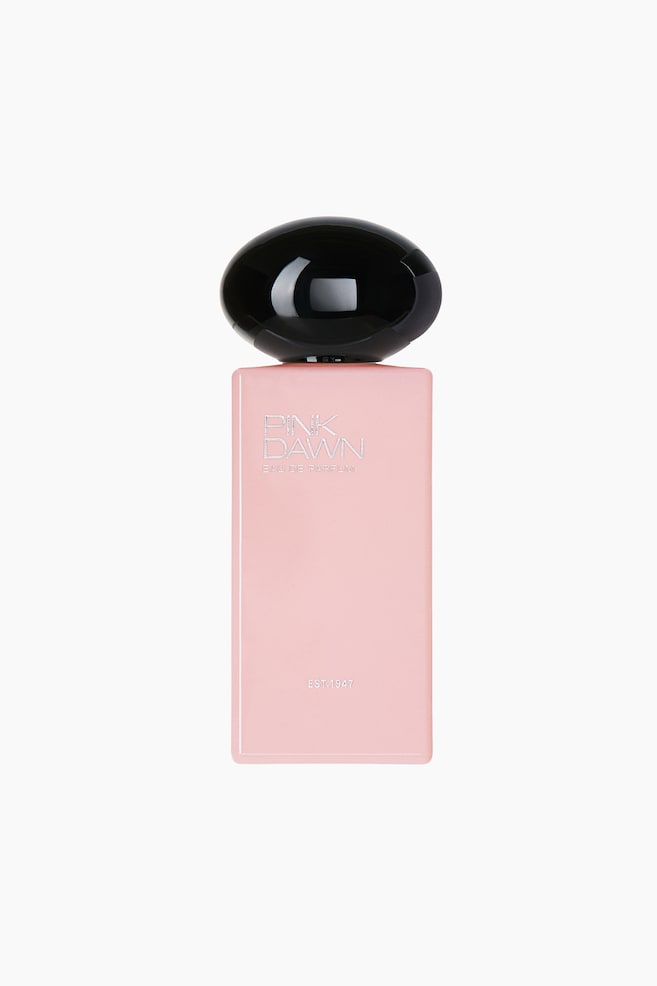 Das Pink Dawn Eau De Parfum ist in einer frontalen Ansicht zu sehen und verfÃ¼gt Ã¼ber einen rechteckigen, mattrosa Flakon mit einer groÃen, glÃ¤nzenden, abgerundeten schwarzen Kappe. Silberne Schrift auf der oberen Vorderseite des Flakons zeigt âPINK DAWN EAU DE PARFUMâ, wÃ¤hrend die Aufschrift âEST. 1947â sich nahe dem unteren Rand befindet. - 1