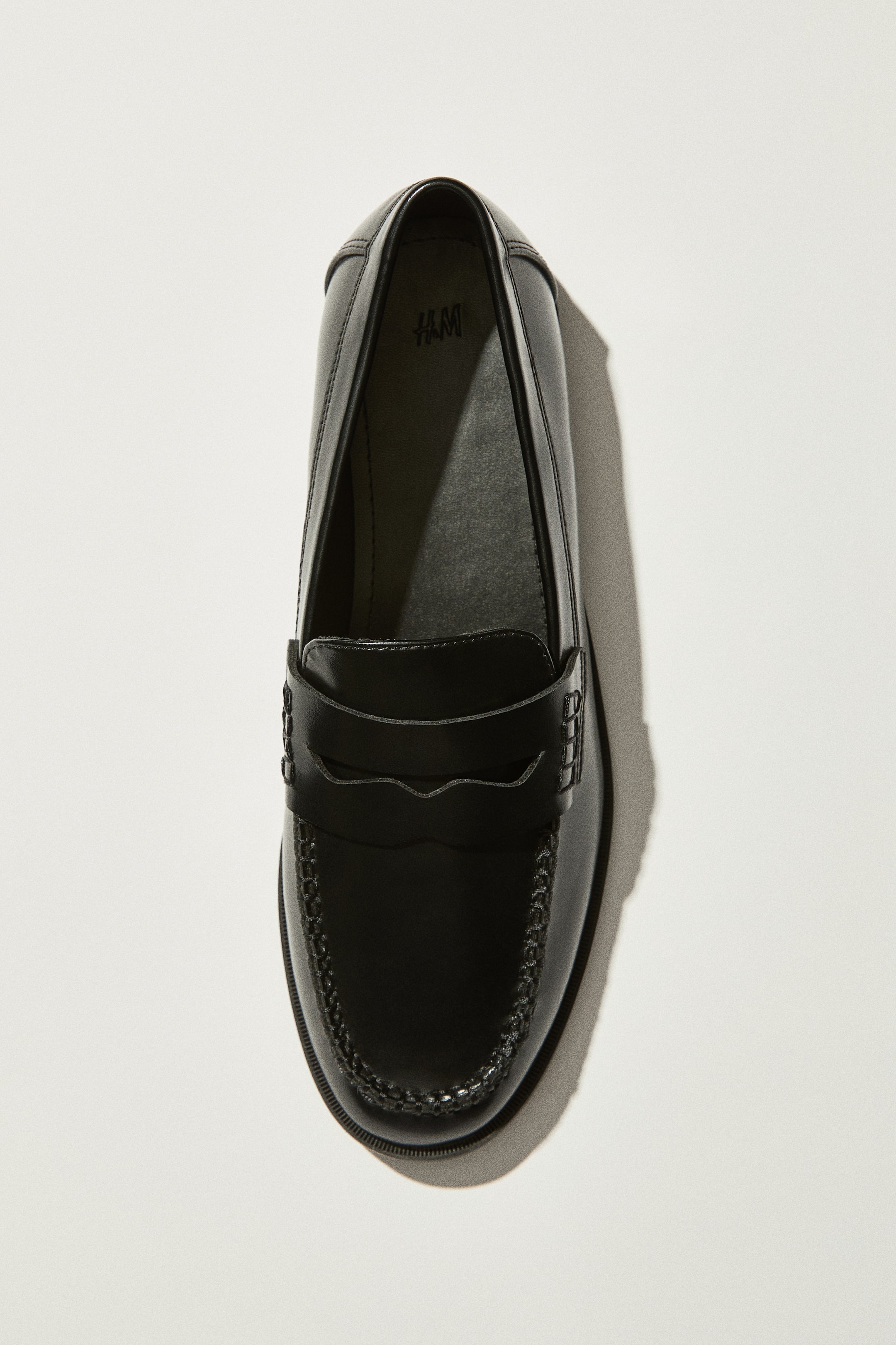 View larger image: A black loafer is positioned facing forward and showcased from a top-down perspective. It features a moccasin seam encircling the toe box and a penny keeper strap traversing the vamp.