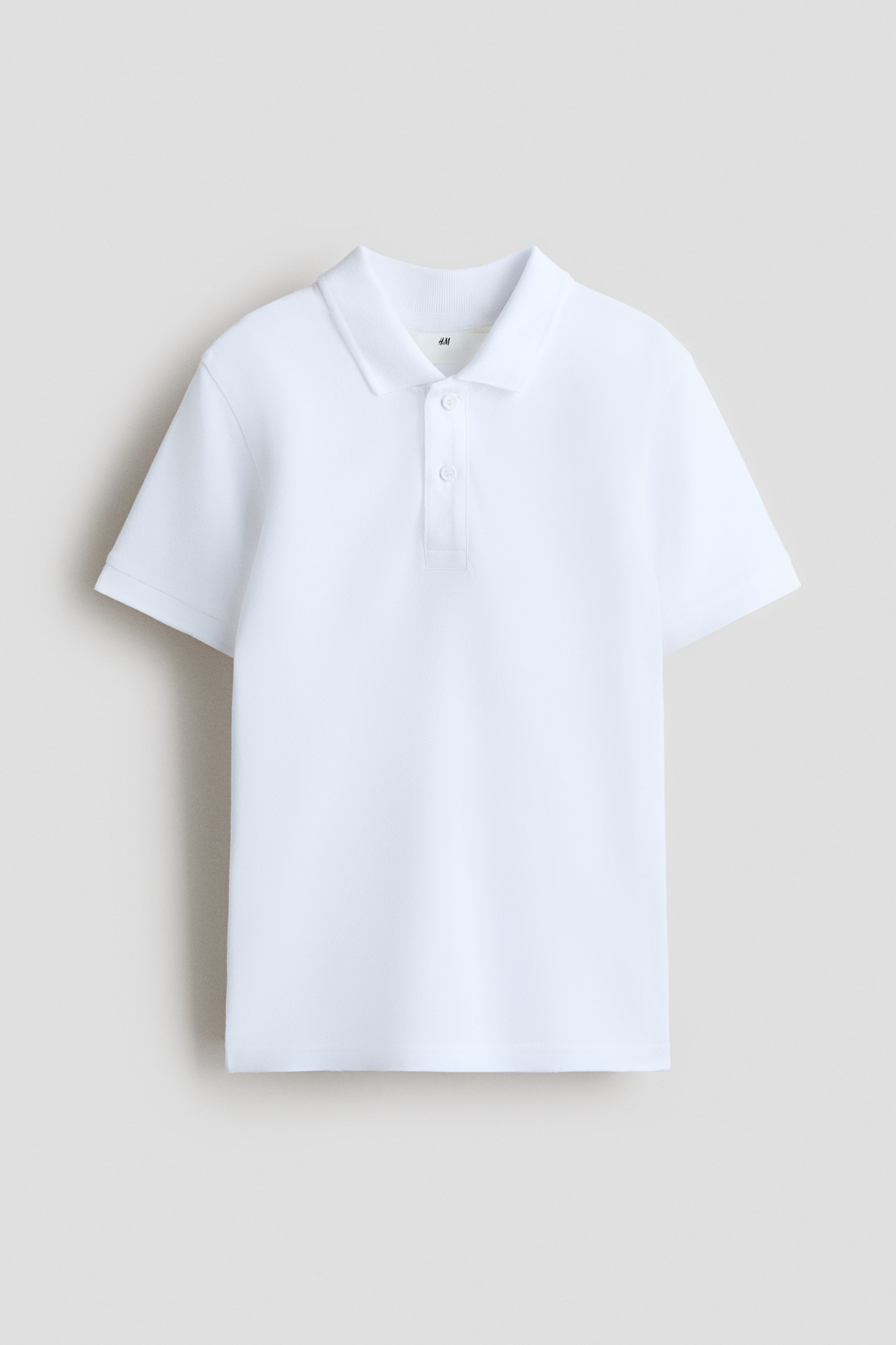 View larger image: A white pique knit polo shirt is lying flat, facing forward. It features a pointed collar, a two-button placket with white buttons, short sleeves with ribbed cuffs, and a straight hem.