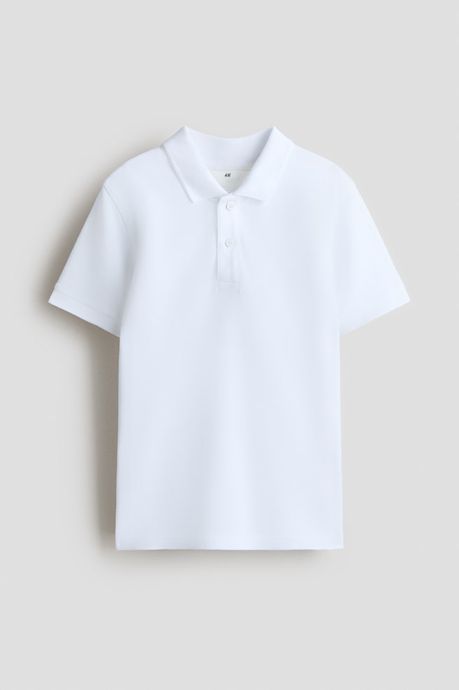Ein weißes Piqué-Strick-Poloshirt liegt flach und zeigt die Vorderseite. Es verfügt über einen spitzen Kragen, eine Zwei-Knopf-Leiste mit weißen Knöpfen, kurze Ärmel mit gerippten Bündchen und einen geraden Saum. - 1