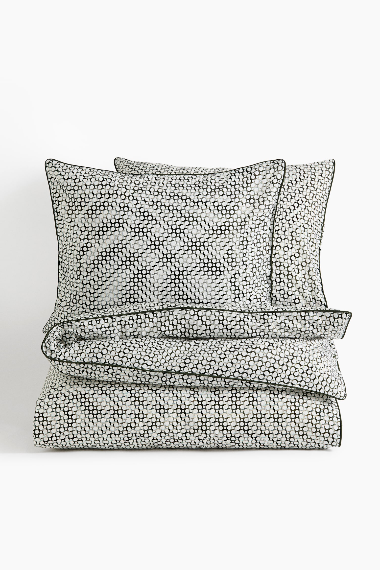 A bedding set is featuring a neatly folded duvet cover and two upright pillowcases, all showcasing a small, repeating black-and-white geometric grid pattern. Each item is displaying dark green piped edges, with the set arranged facing the front. - 1