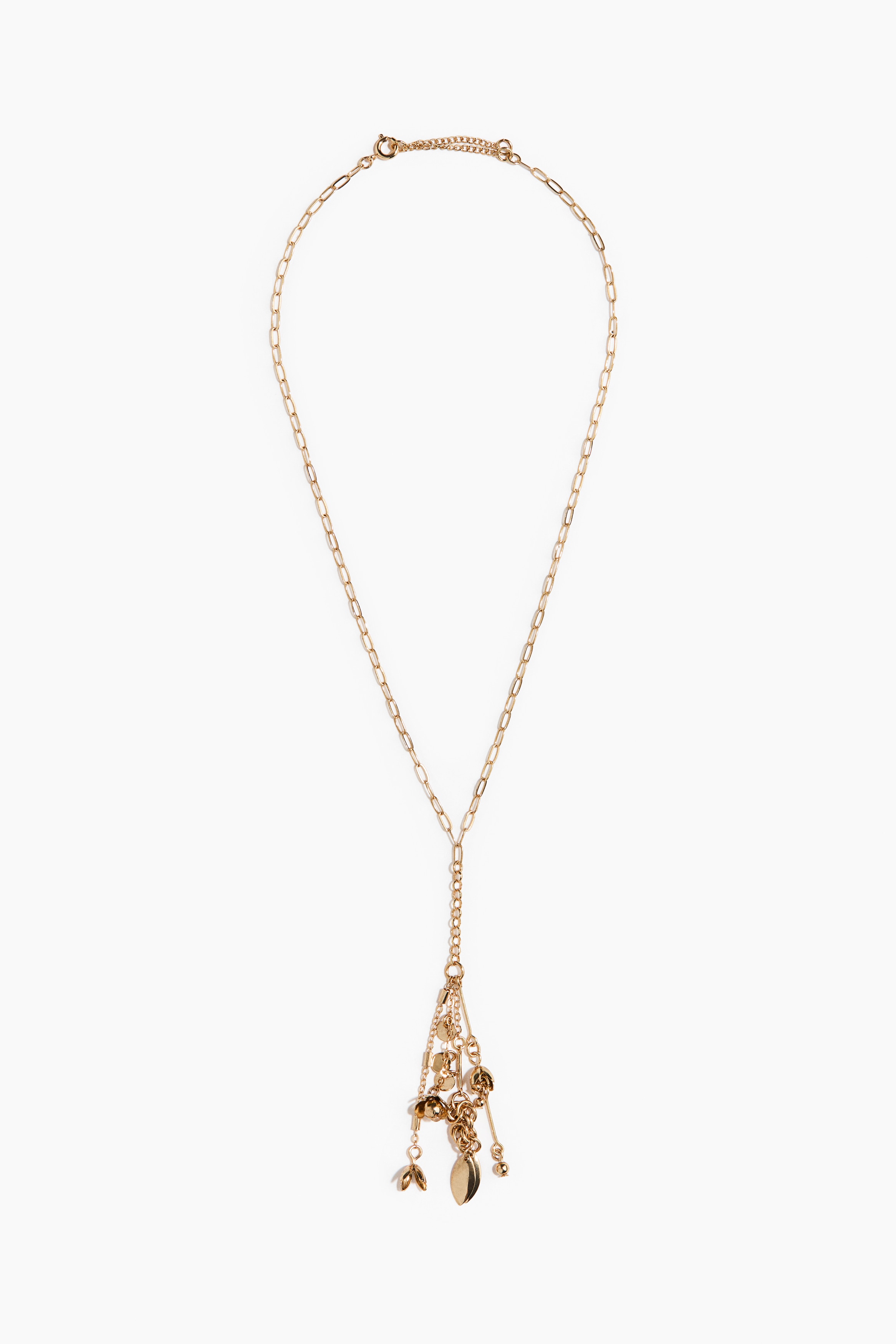 Een lariatketting in goudtint met een paperclip-metaalketting en bungelende bedeltjes wordt gedragen door het model. De ketting is gelaagd over een crÃ¨mekleurige kanten top en omlijst door een open, sterk gestructureerd crÃ¨mekleurig jack.