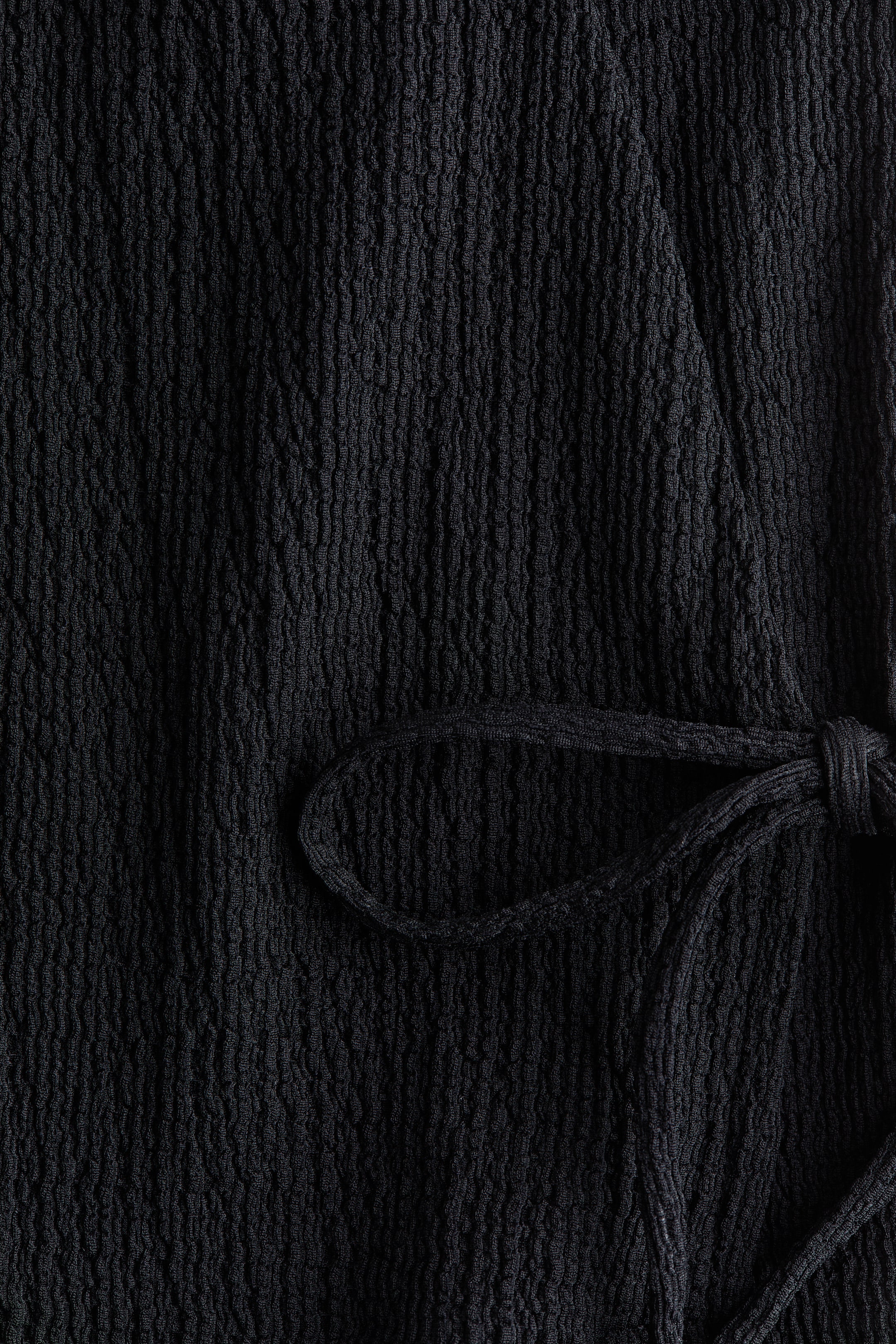 Agrandir l'image: Un tissu noir présente une texture froissée distincte, avec une fermeture à nouer créant un nœud et une boucle sur la droite.