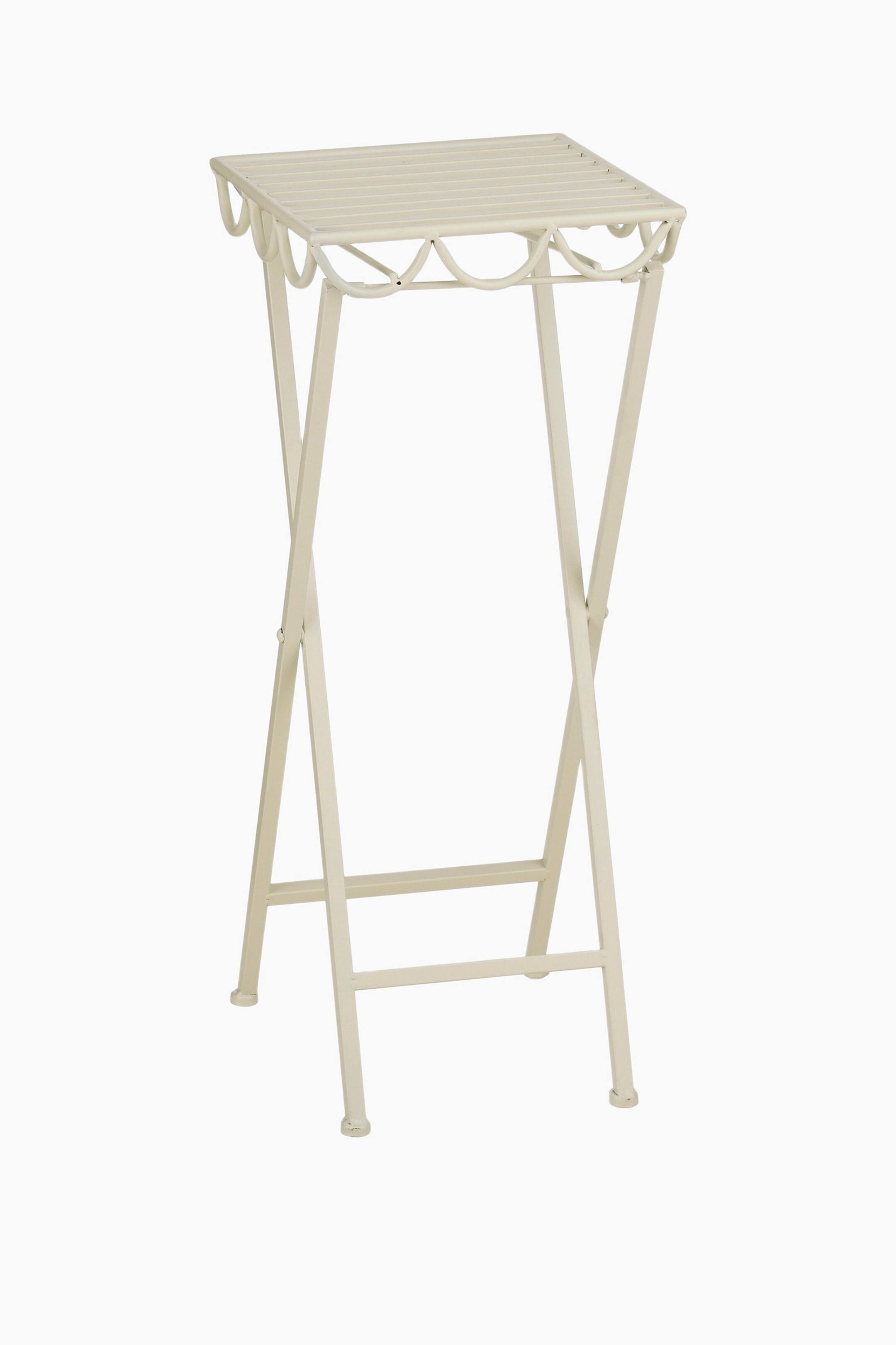 Agrandir l'image: Un support pour plantes en métal de couleur crème est légèrement orienté vers l'avant, avec un dessus carré à lattes orné d'une bordure décorative festonnée en dessous, et quatre pieds en forme de X reliés par des barres transversales horizontales près du bas.