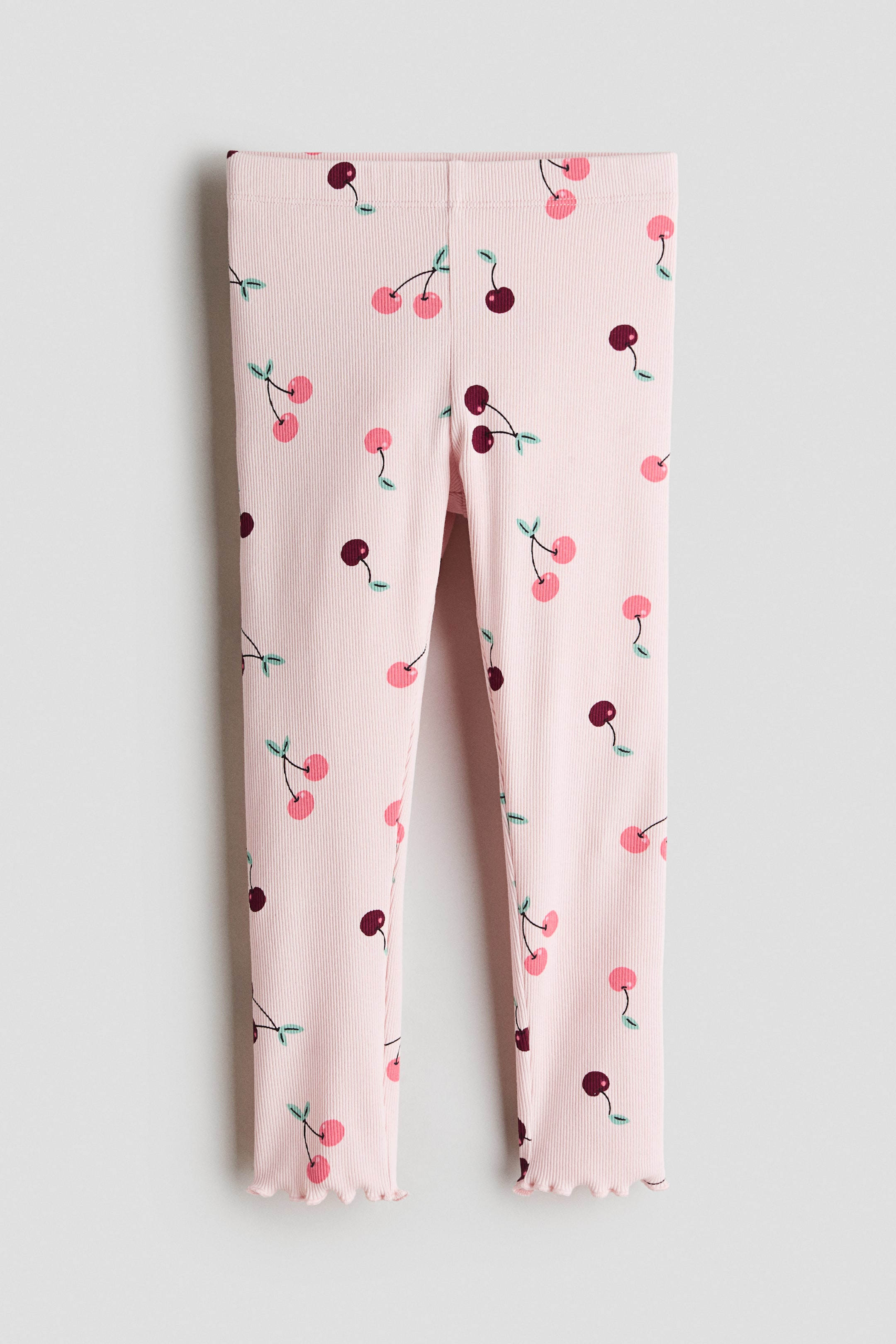 Xem ảnh lớn hơn: Quần legging dệt kim gân màu hồng có họa tiết in quả anh đào, nổi bật với những quả anh đào màu hồng nhạt và đỏ đậm cùng cuống màu xanh, được hoàn thiện với đường viền bèo nhún ở mắt cá chân.