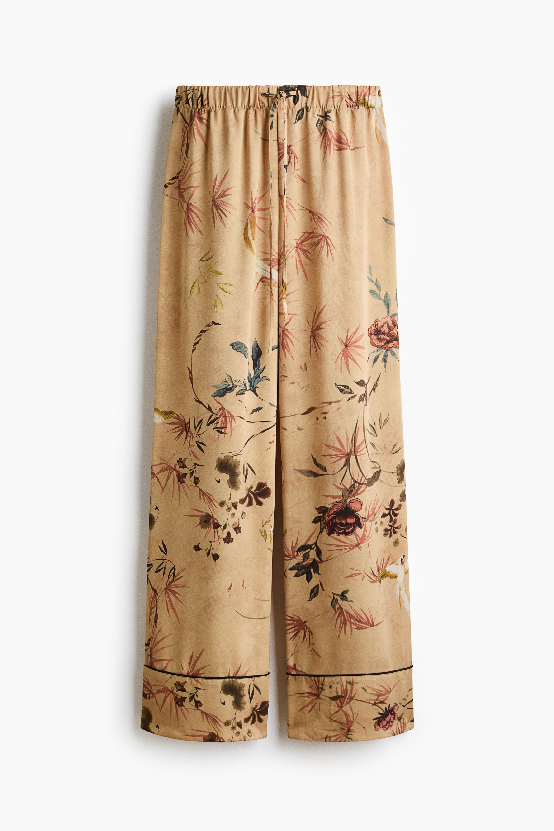 Il modello indossa pantaloni in tessuto fantasia con stampa botanica, vita elasticizzata con coulisse e gamba dritta con orli rifiniti con profili. I pantaloni sono abbinati a una camicia coordinata a maniche lunghe con stampa botanica.