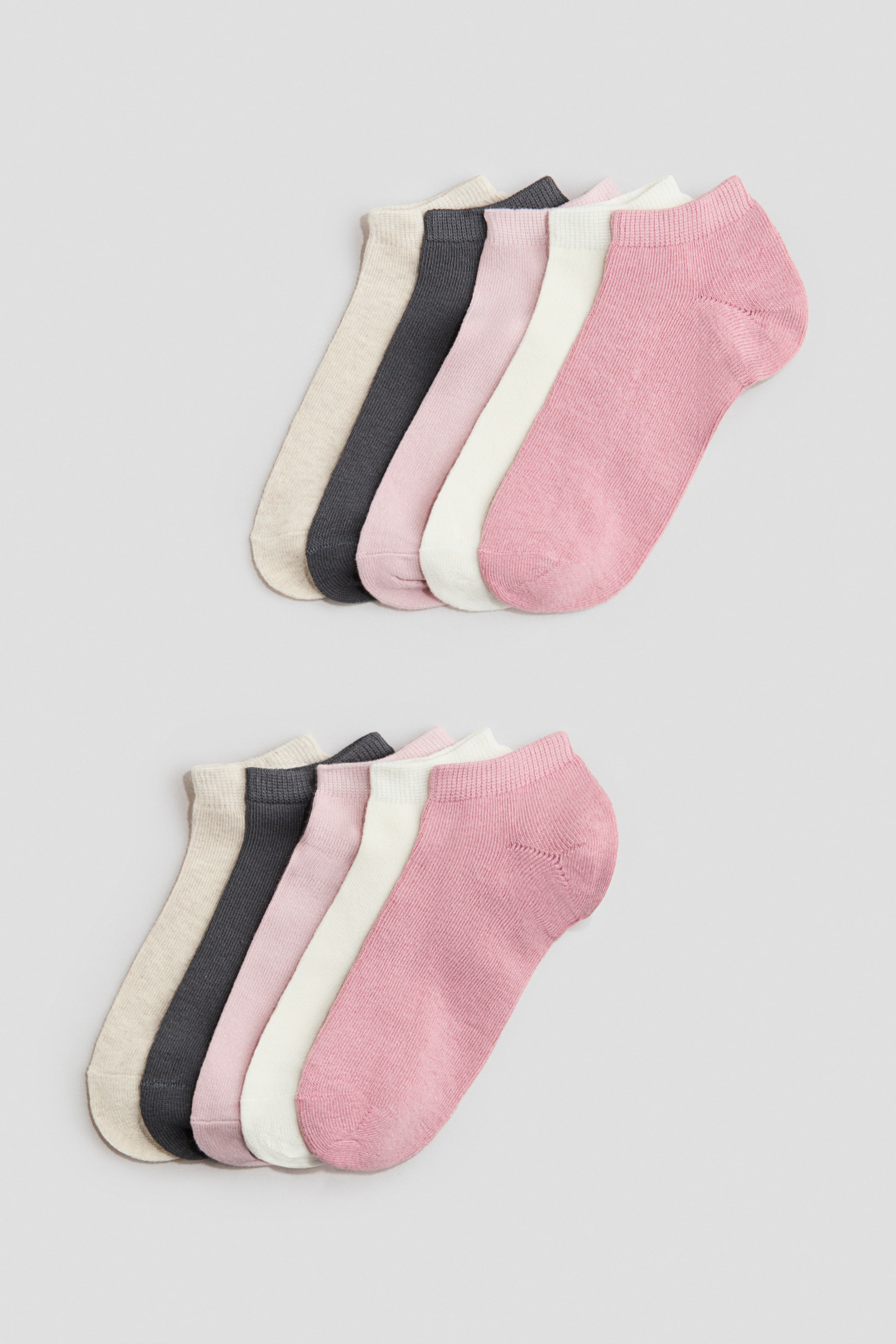 View larger image: Trainer socks are showcased front-facing in two fanned sets, each comprising five pairs. The fine-knit socks exhibit elasticated tops and showcase a variety of colours including beige, dark grey, light pink, off-white, and pink.