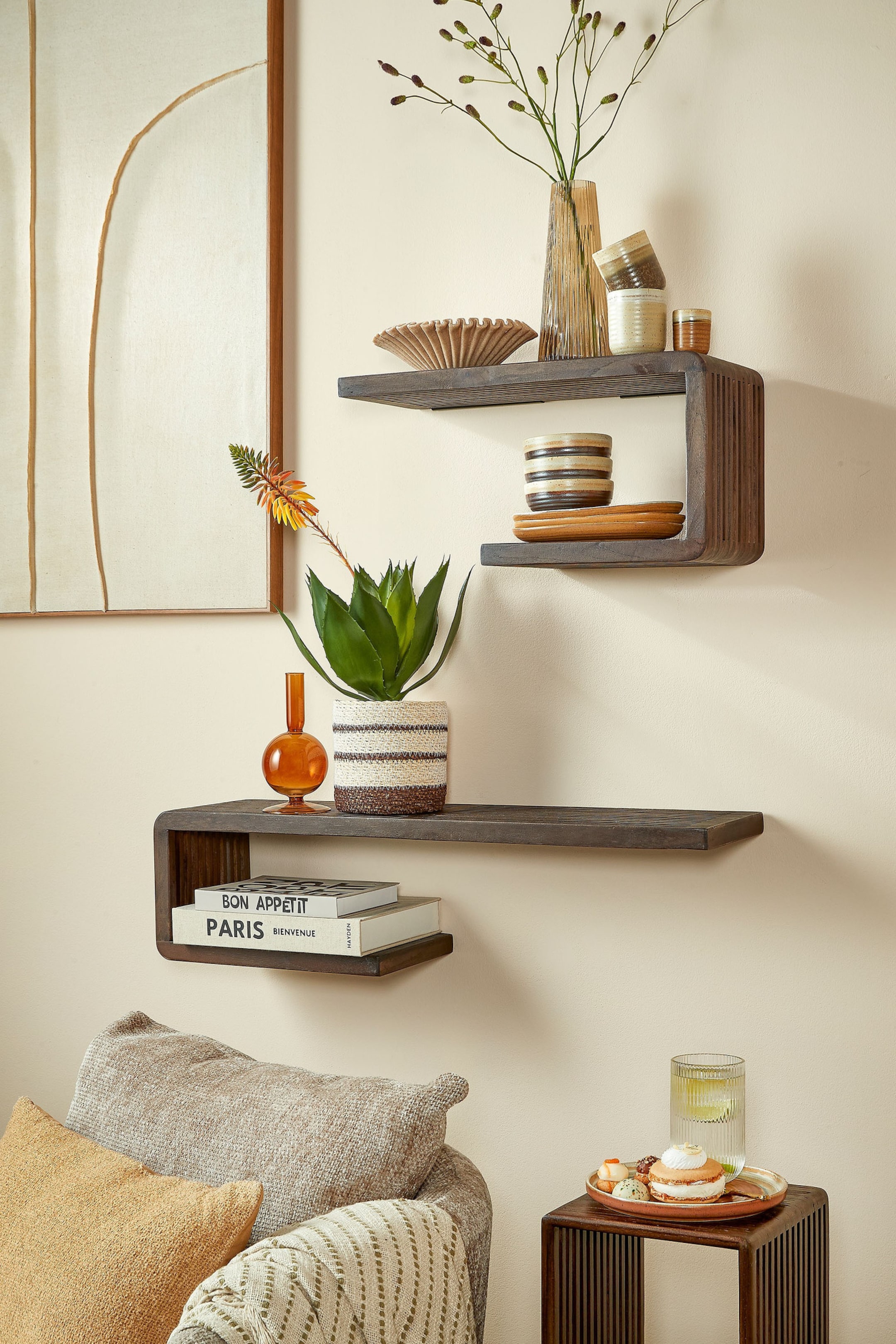 Größeres Bild ansehen: Zwei dunkel gebeizte Holz-Wandregale mit schwebendem Design zeichnen sich durch eine geschwungene Halterung aus. Das obere Regal biegt sich nach rechts unten, während das untere Regal sich nach links unten biegt. Die vertikalen geschwungenen Abschnitte zeigen dezente Riffelungen.
