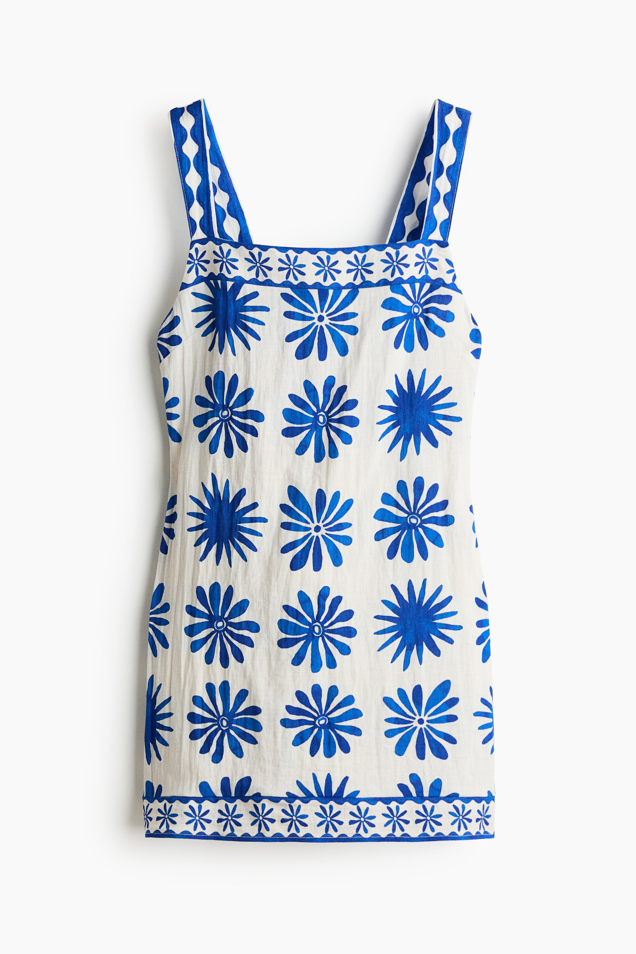 View larger image: A short, fitted dress crafted from a white viscose-blend weave is showcased from the front. It features a square neckline and wide shoulder straps adorned with a blue and white wavy pattern. The overall design includes large blue floral shapes accented by bands of smaller blue starbursts at the neckline and hem.