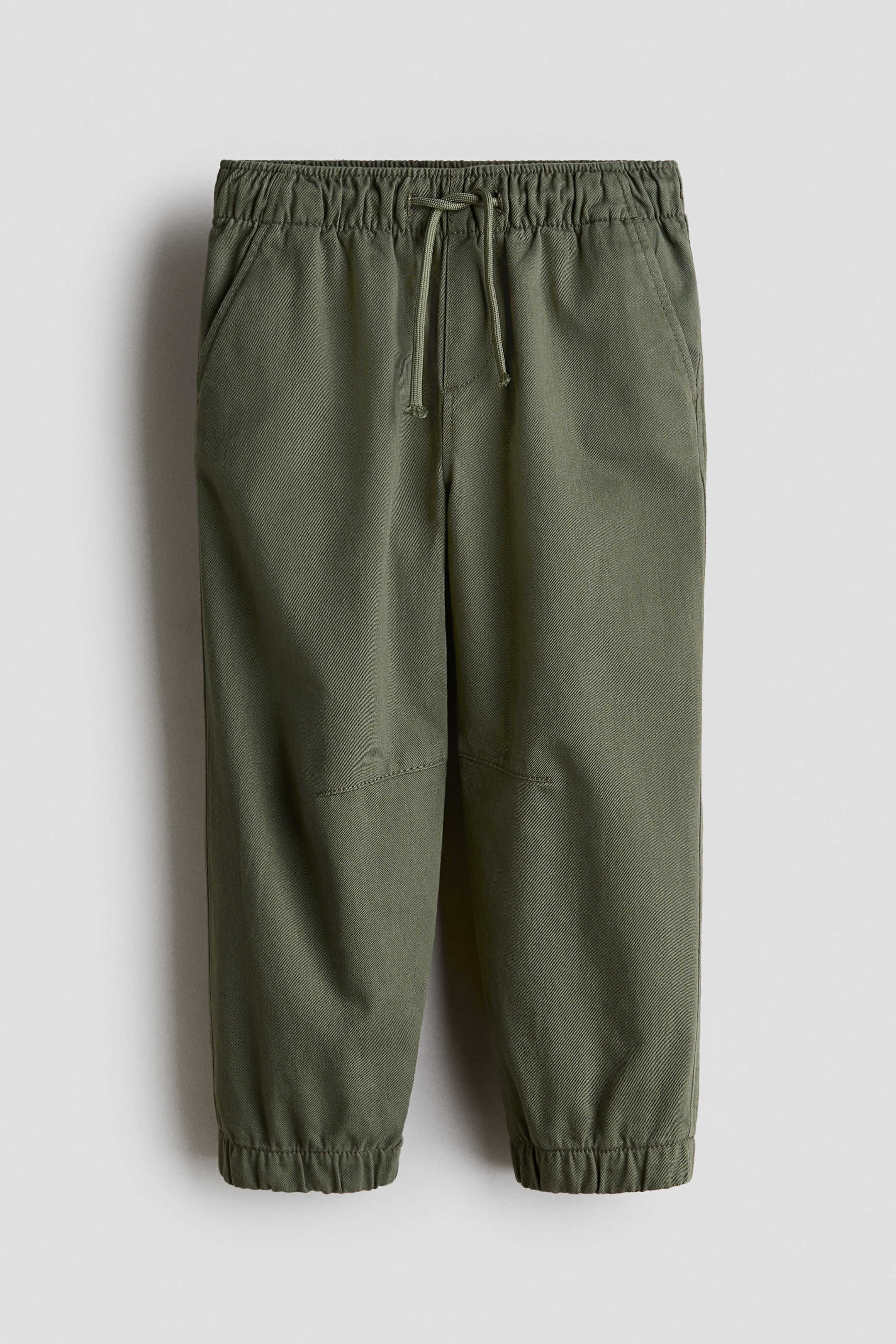 View larger image: Olive green pants come with an elasticised drawstring waistband at the front. They feature side slash pockets, articulated knee panels, and elasticised cuffs.