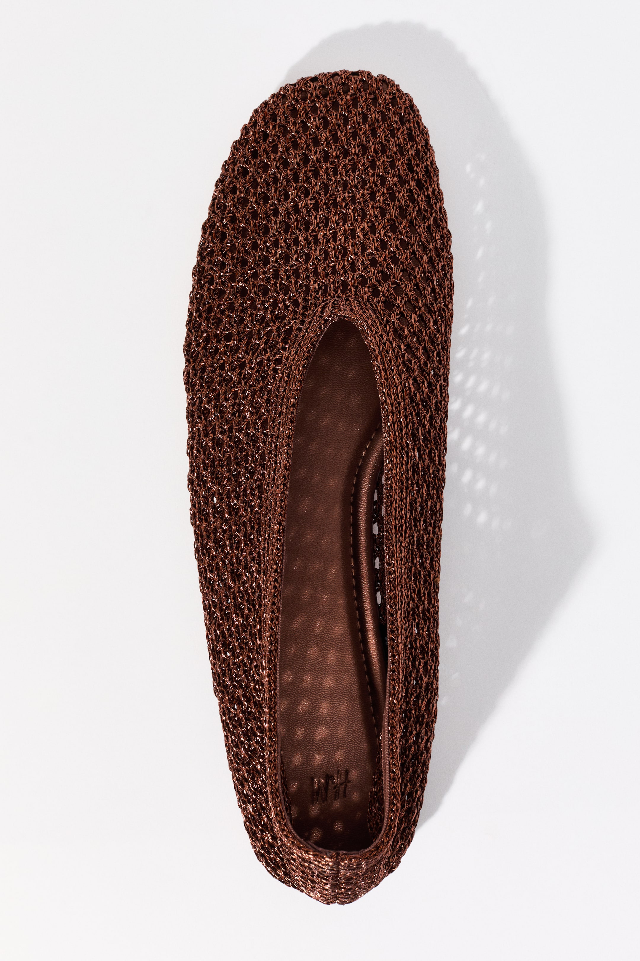 View larger image: The image showcases a brown flat shoe viewed from the top, highlighting a shimmering brown woven mesh upper. The elliptical foot opening reveals a solid brown interior sole with a subtle dotted texture and the 'H&M' logo at the heel.