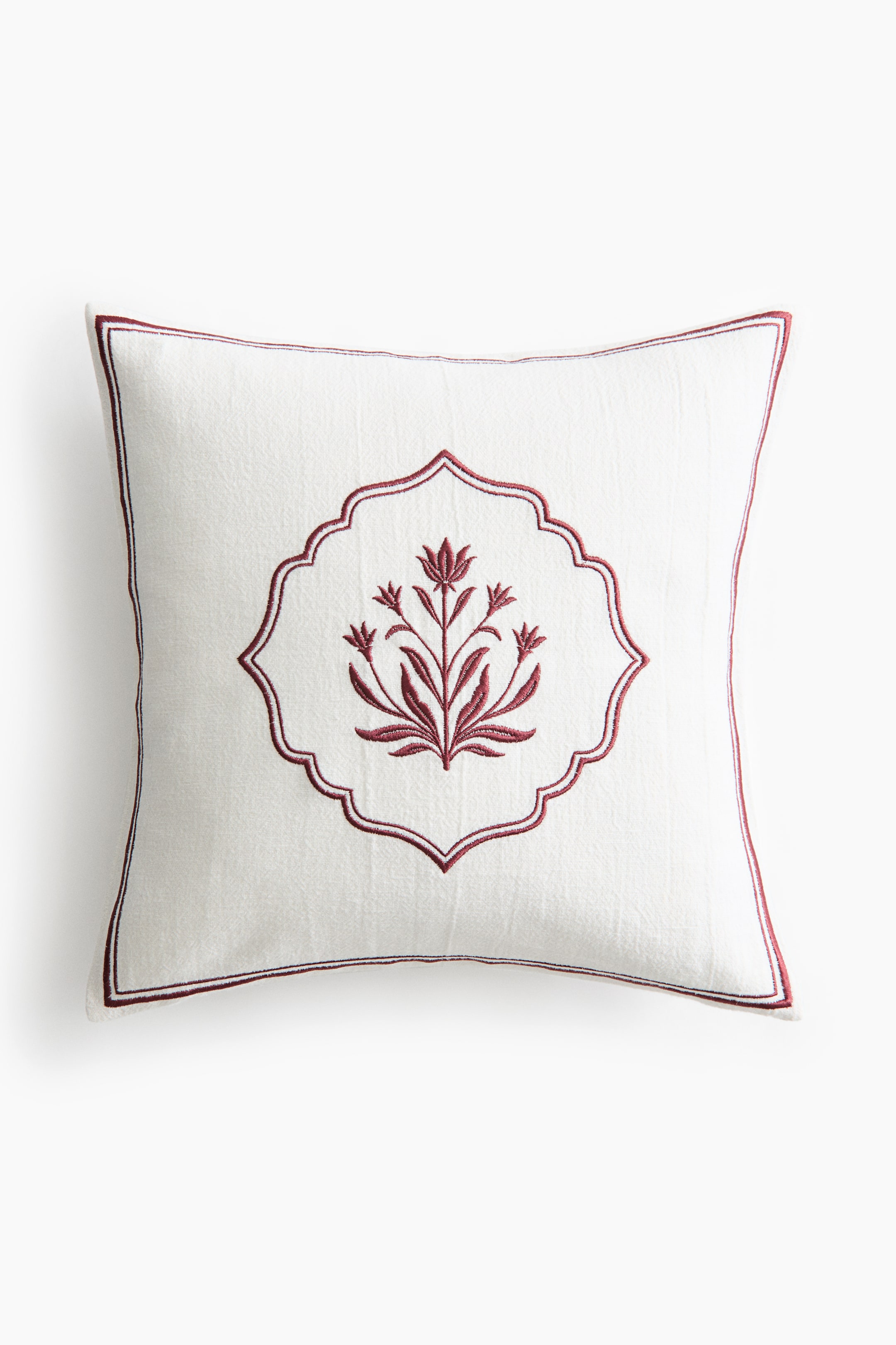 View larger image: A square off-white decorative cushion is facing front, displaying a central dark red embroidered floral motif enclosed within a scalloped frame. A thin dark red embroidered border frames the outer edges of the textured fabric.
