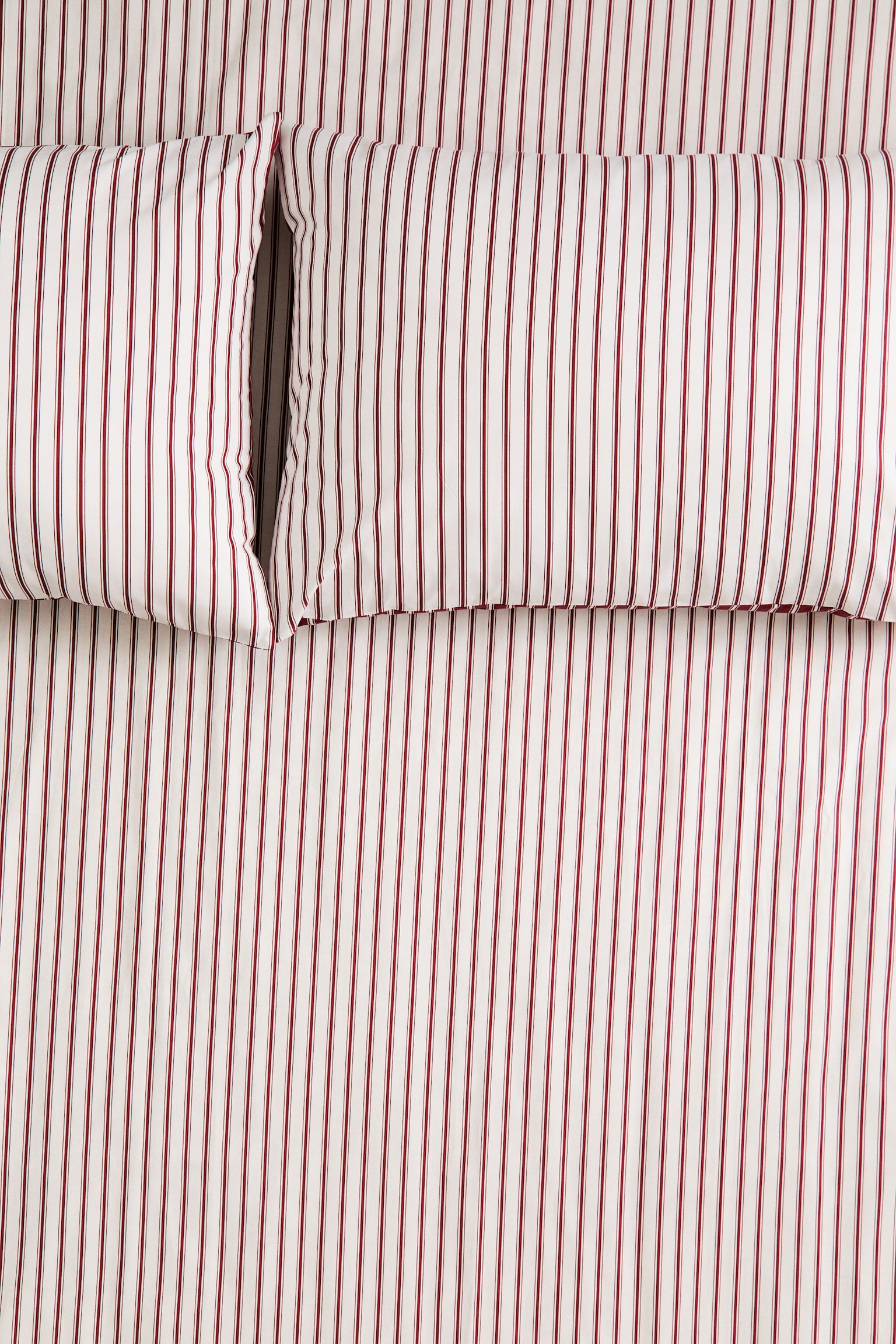 A bedding set featuring white fabric with red vertical ticking stripes is shown from an overhead view. The set includes two matching pillows placed side by side at the top, with the striped pattern continuing seamlessly across the pillows and the underlying sheet.