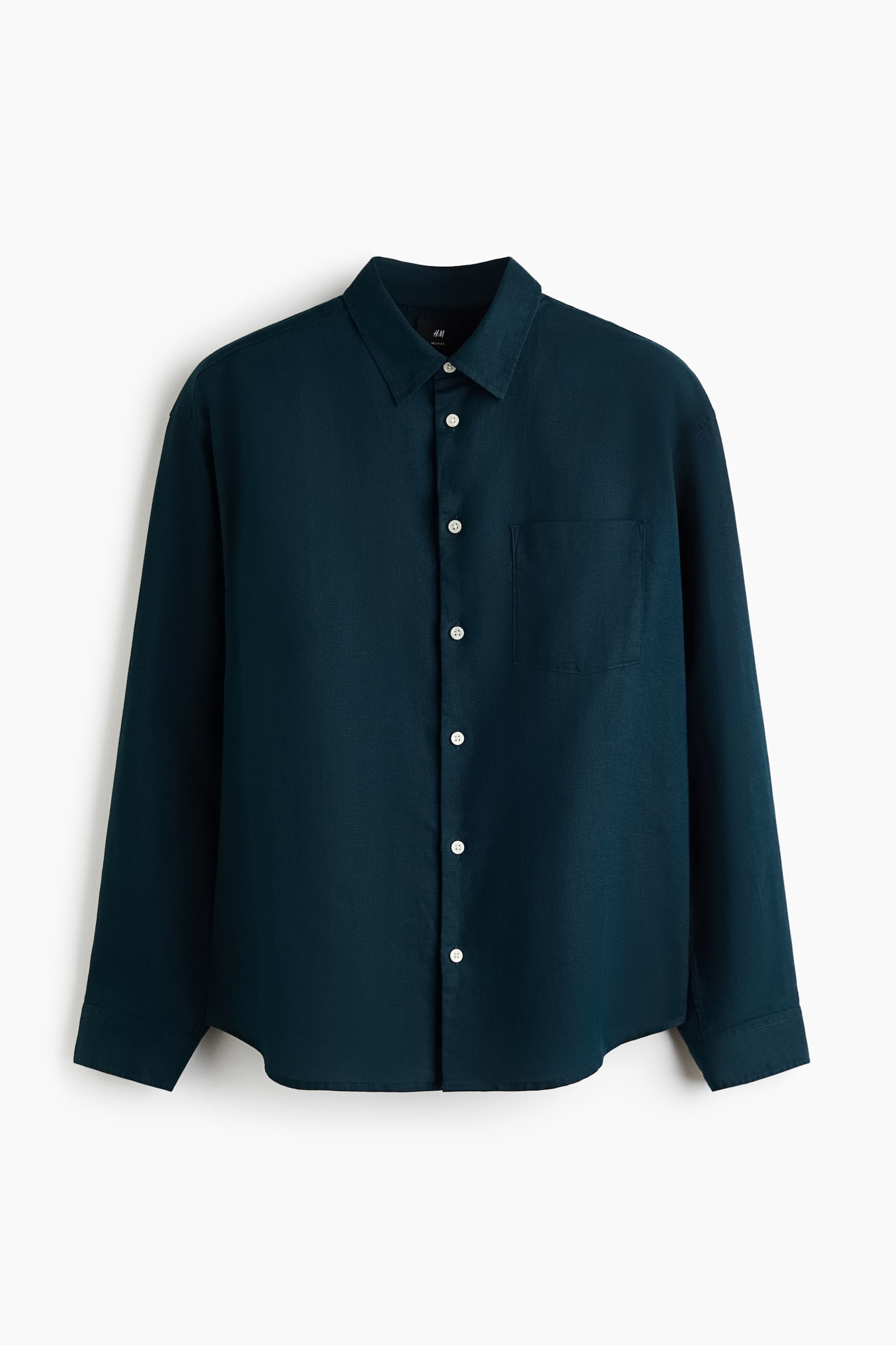 A dark teal, long-sleeved shirt in a textured cotton and linen blend is hanging facing forward. It features a turn-down collar, a French front with contrasting white buttons, a single open chest pocket, and a slightly rounded hem.
