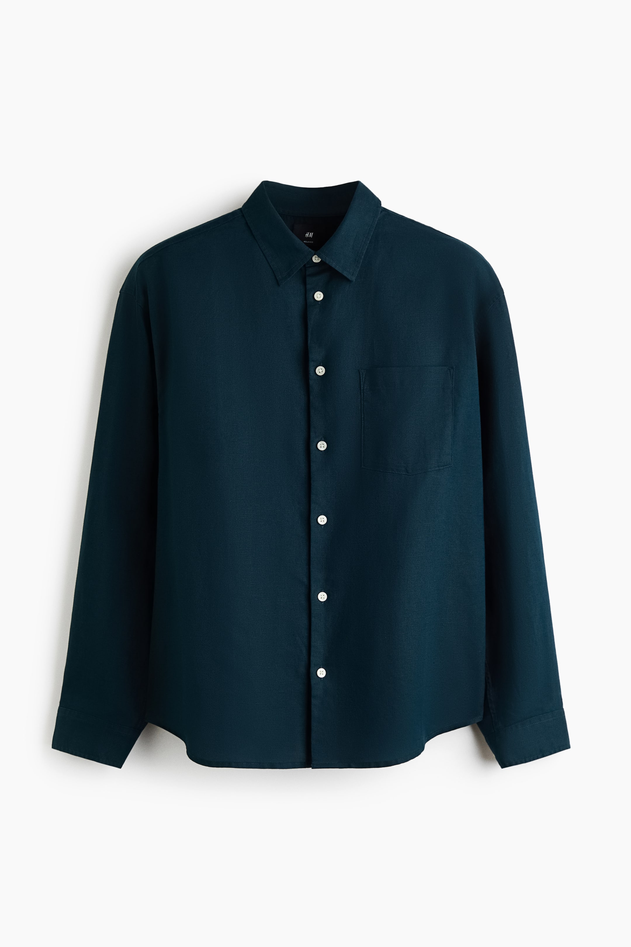 View larger image: A dark teal, long-sleeved shirt in a textured cotton and linen blend is hanging facing forward. It features a turn-down collar, a French front with contrasting white buttons, a single open chest pocket, and a slightly rounded hem.
