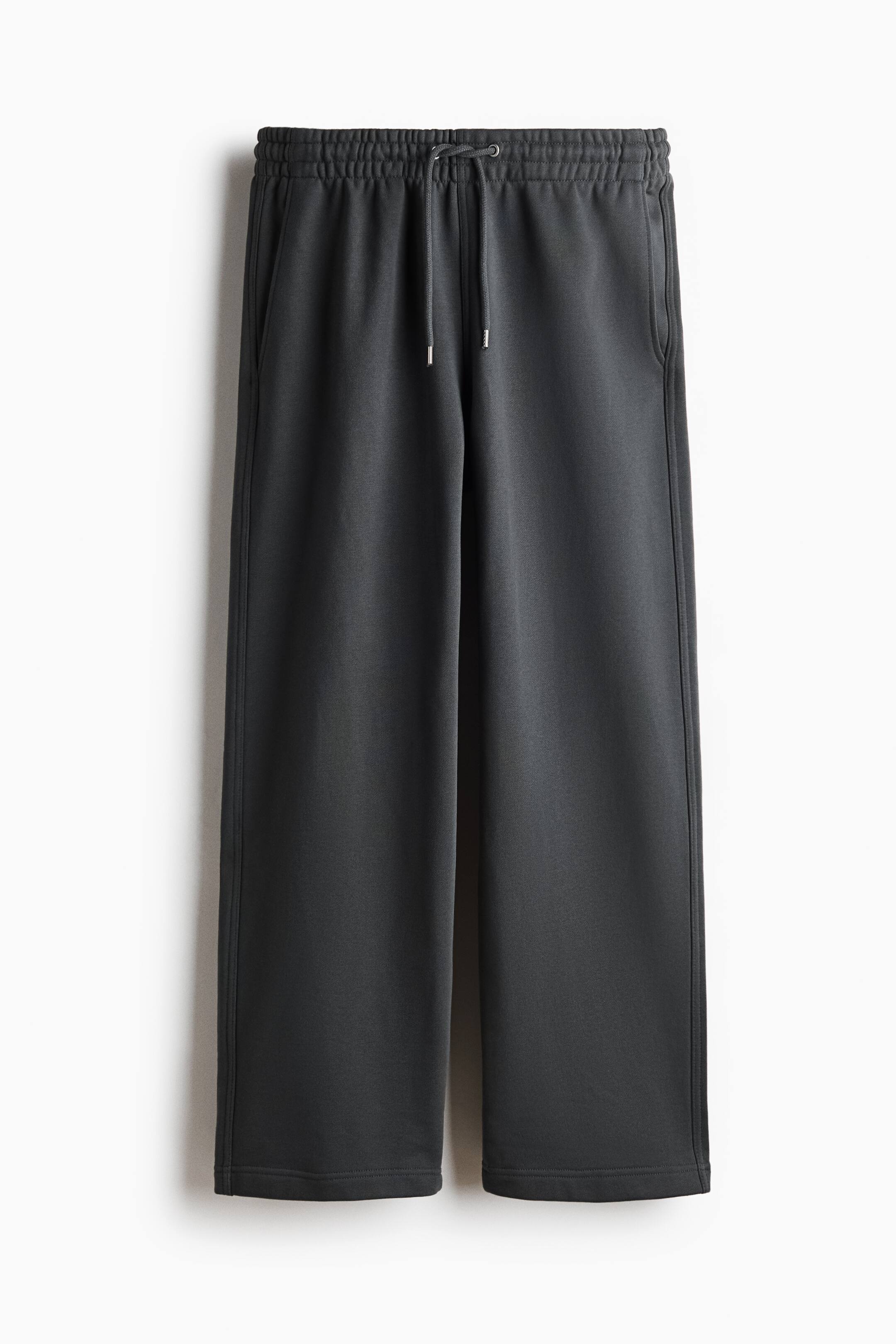 View larger image: Dark grey sweatpants are shown from the front, made of a smooth cotton sweatshirt fabric. They feature a covered elasticated waistband with a visible drawstring, and side pockets. The legs are cut in a loose, straight fit.