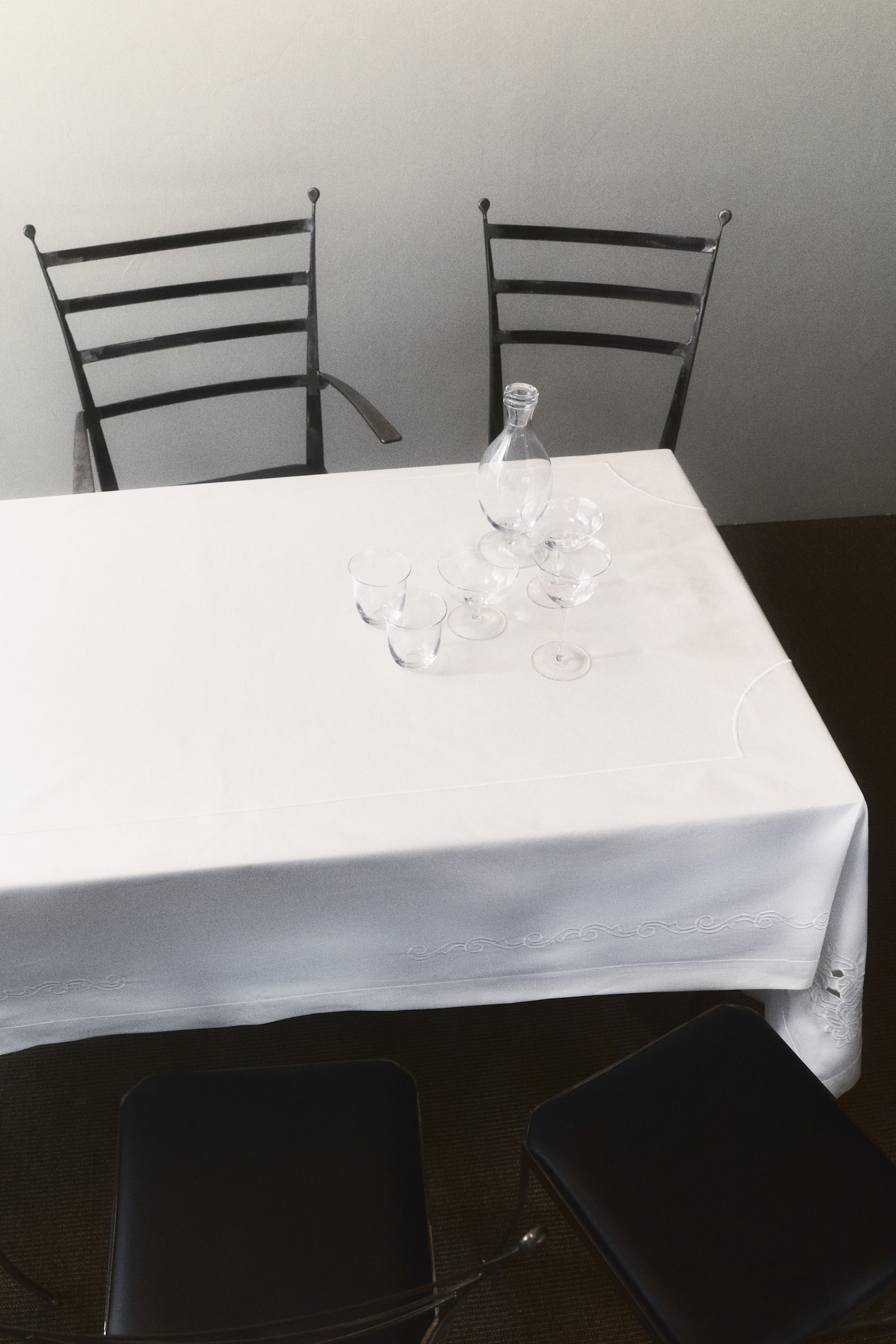 A white embroidered textile is lying flat, presenting front-facing. It is featuring intricate white embroidery on one corner, which is extending along two edges with scrollwork, floral motifs, and delicate cut-outs, and is displaying a neatly hemmed border. - 1