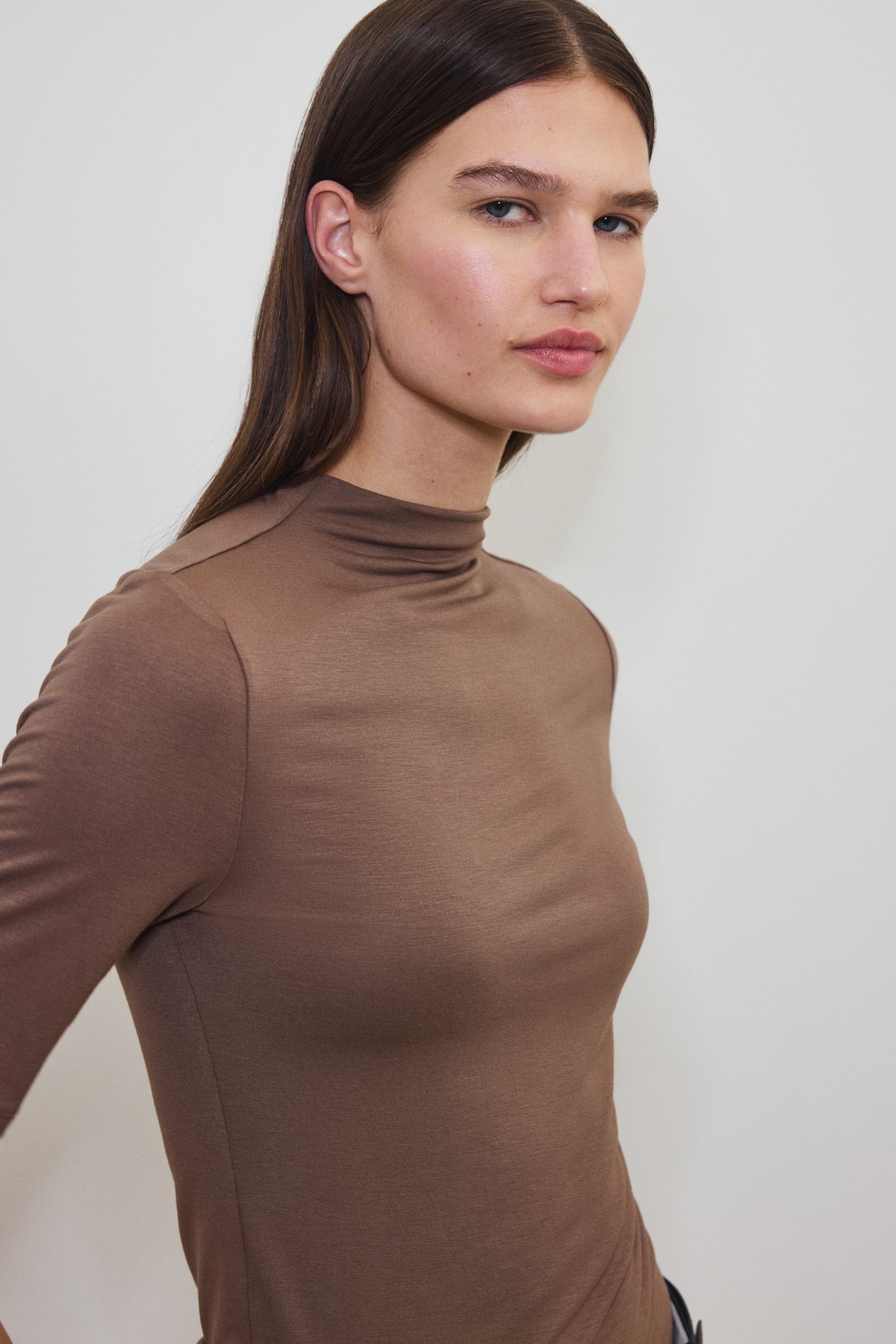 View larger image: A brown long-sleeve T-shirt with a turtleneck fits snugly on the model's upper body. The model is wearing the T-shirt, crafted from a fabric that appears soft.