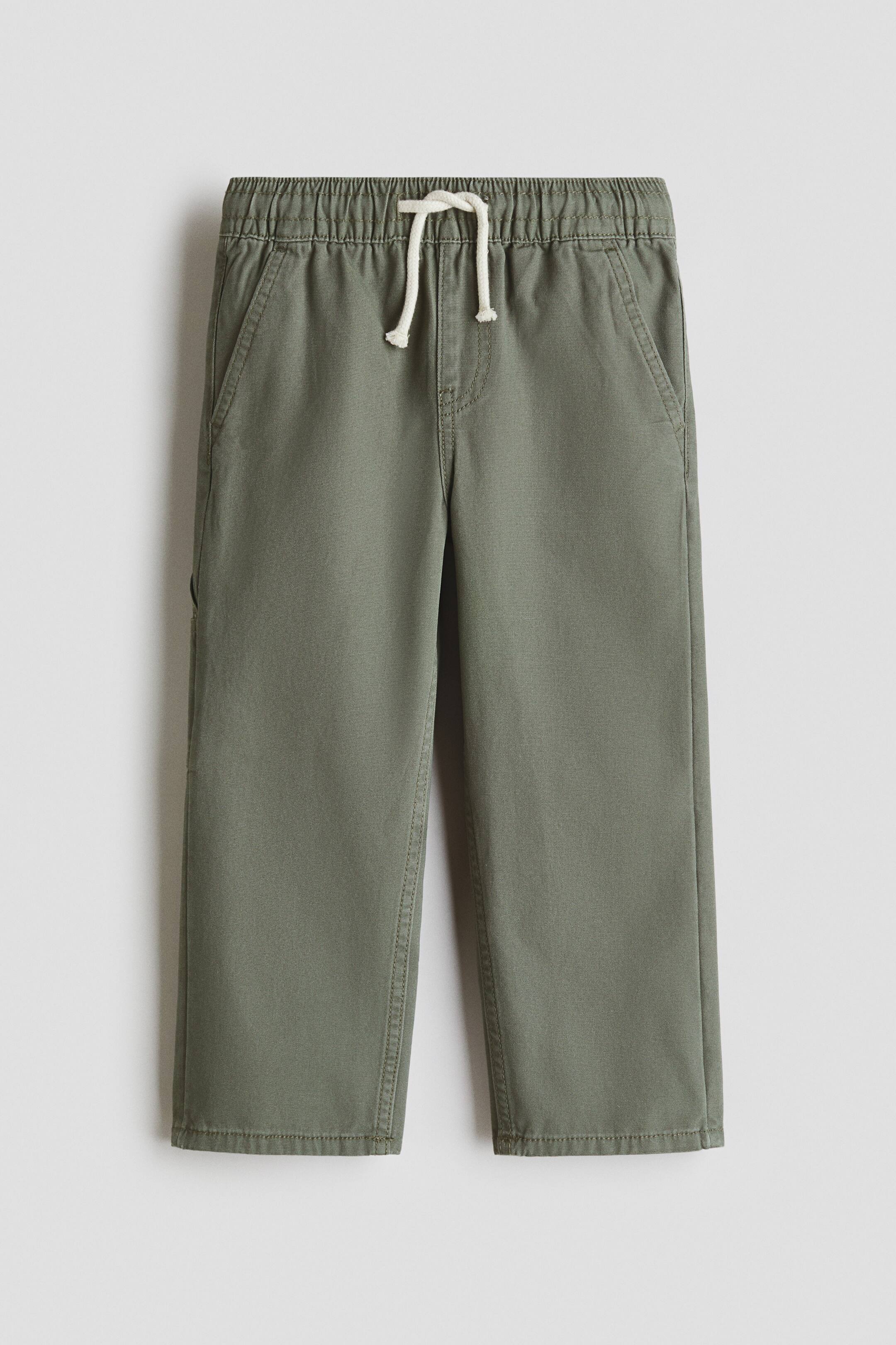 View larger image: Olive green trousers boast an elasticated waistband with a white drawstring tied in a knot. They feature slanted front pockets, a small utility pocket on the left side, and straight legs with stitched hems.