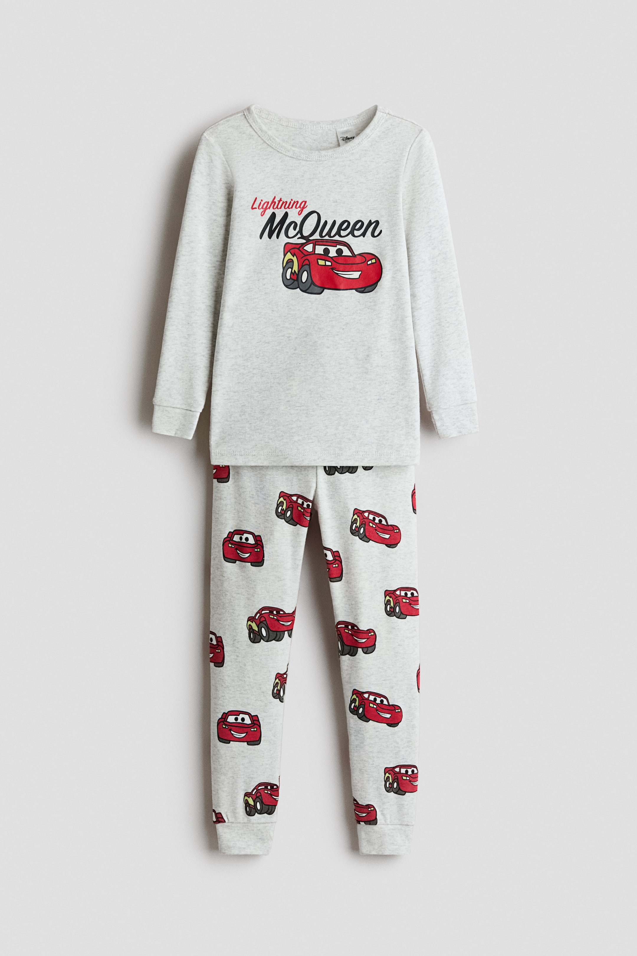 View larger image: A front-facing view shows a light gray marl pajama set consisting of a long-sleeved top and matching pants. The top features a central graphic print of the red car character Lightning McQueen, while the pants display an all-over print of the same character and cuffed hems.