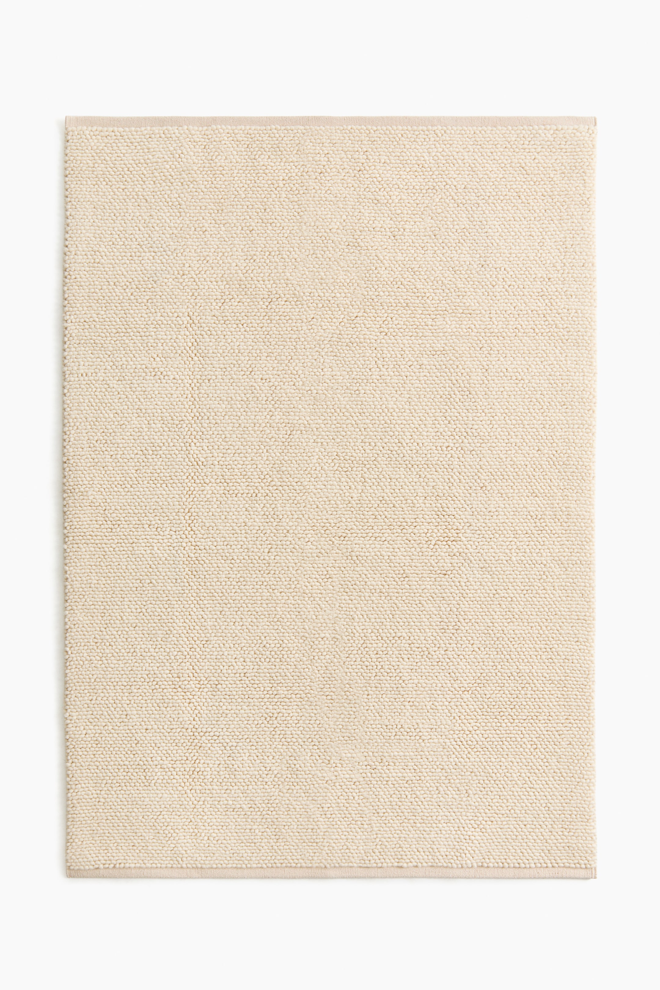 Agrandir l'image: Un tapis rectangulaire beige clair présente son devant. Sa surface affiche un tissage texturé et bouillonnant, et ses bords apparaissent soigneusement finis.