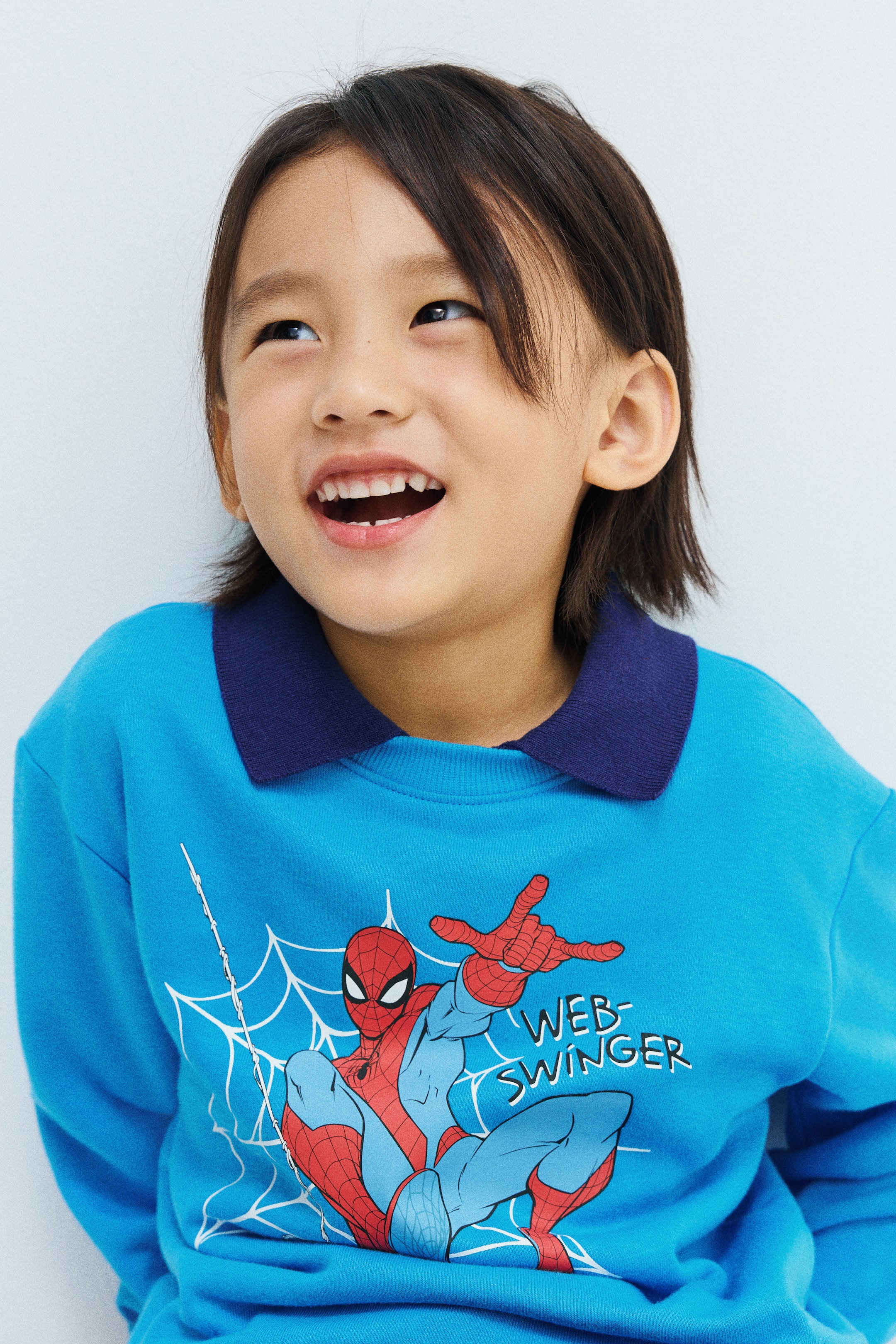 이미지 확대 보기: 모델이 전면에 프린트된 스파이더맨 그래픽이 돋보이는 블루 스웨트셔츠를 착용하고 있습니다. 이 스웨트셔츠는 라운드 넥과 립 처리된 넥라인, 드롭 숄더 디테일이 특징이며, 진한 블루 컬러의 칼라 위에 레이어드되어 있습니다.