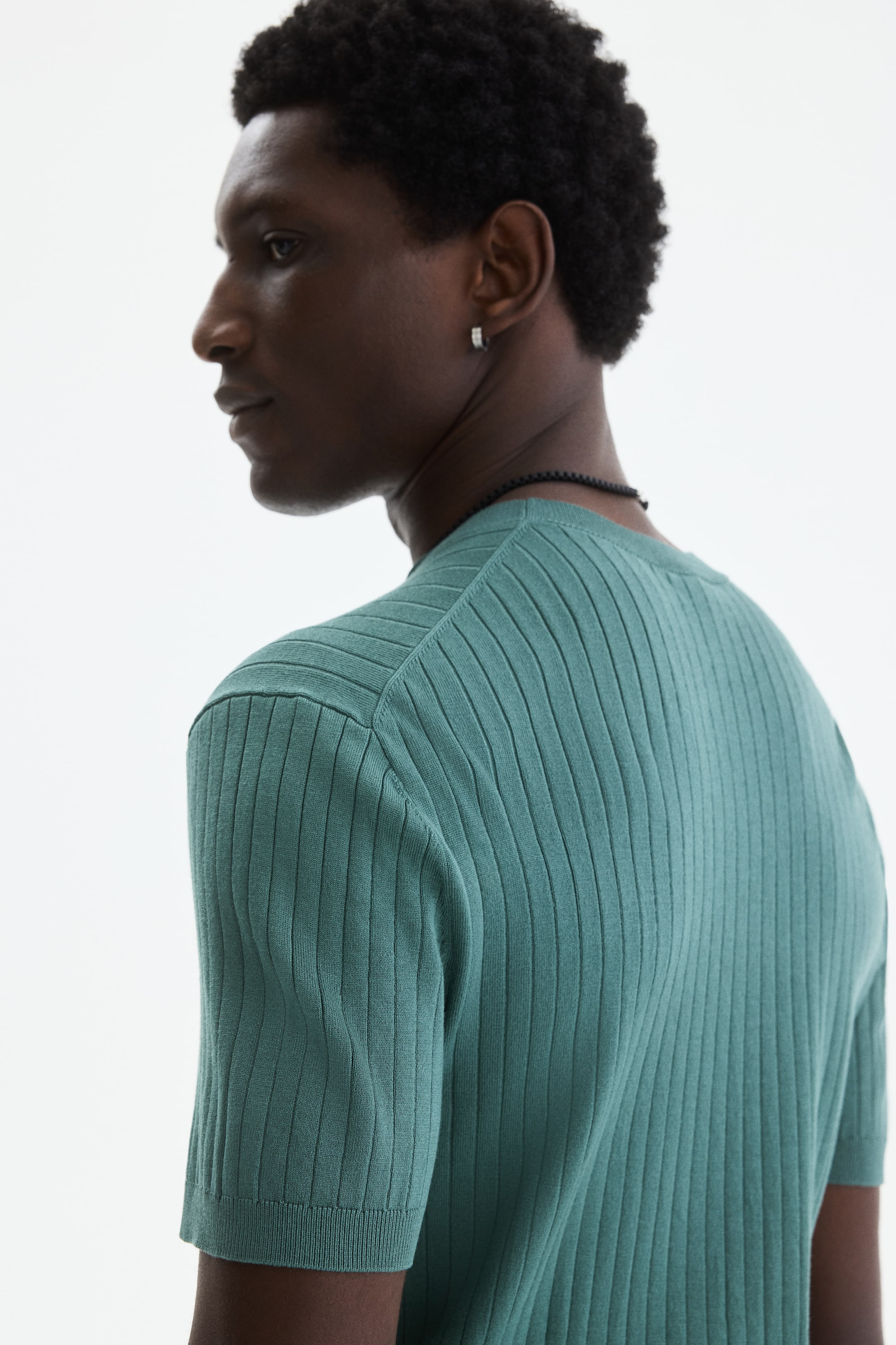 View larger image: A green ribbed knit short-sleeved top is being worn, viewed from the back and side, revealing its close fit. It is displaying a crew neck and ribbed short sleeves.
