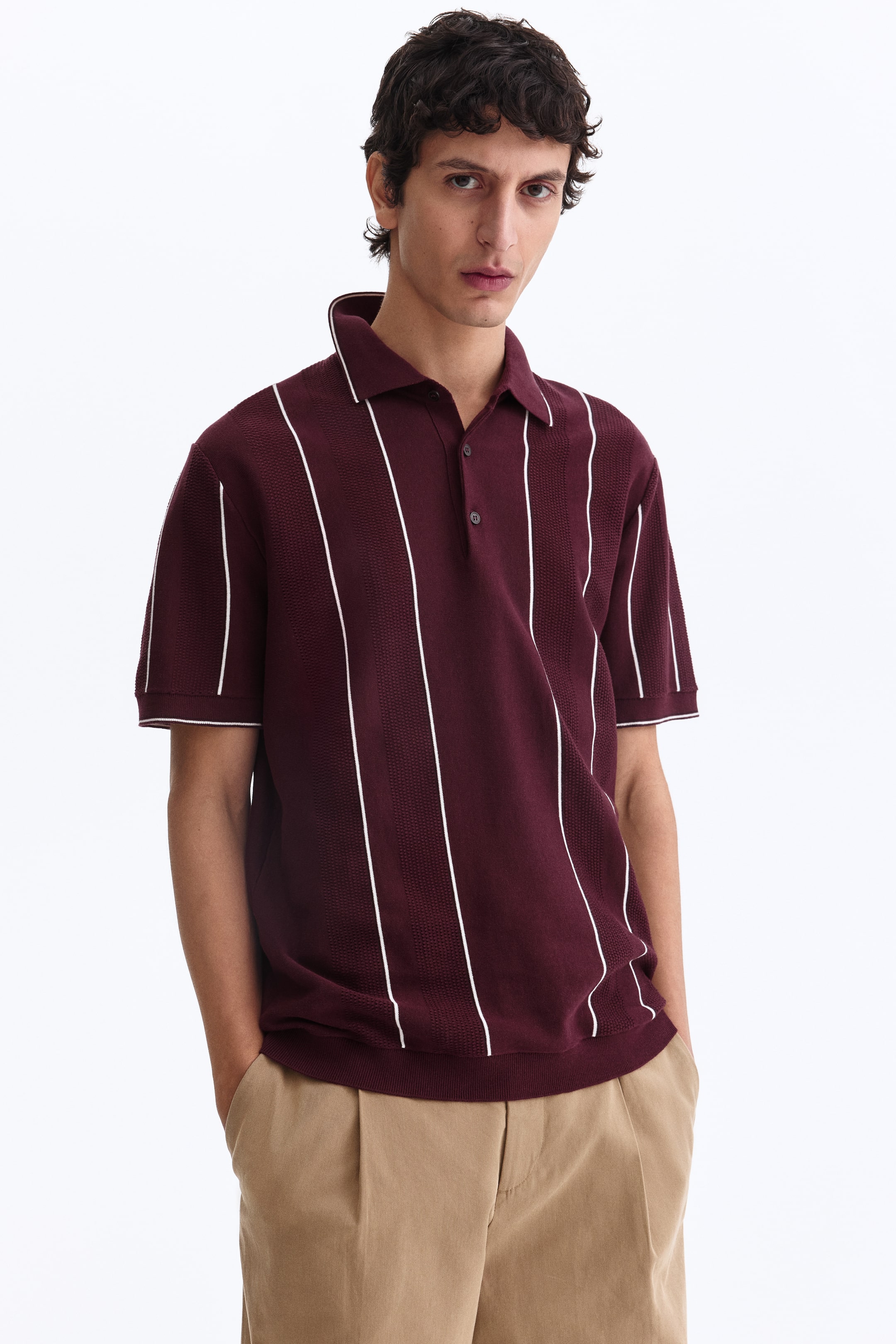 View larger image: Front-facing maroon knit polo shirt featuring white vertical stripes and an overall textured pattern. It is styled with a polo collar, a two-button placket, short ribbed sleeves and a ribbed hem. Both the collar and sleeve cuffs are finished with white piping.