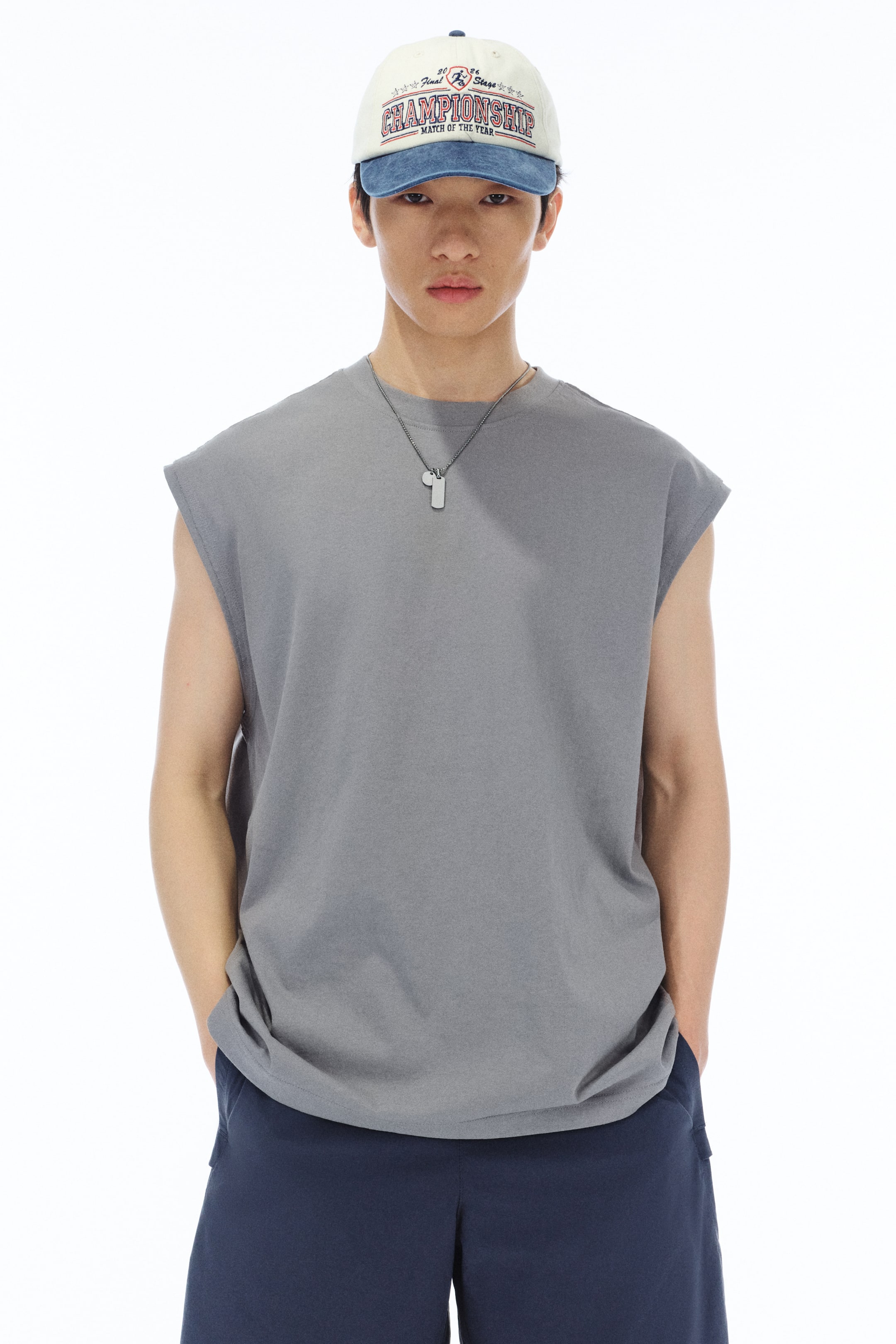 View larger image: The model is showcasing a grey vest top crafted from heavyweight cotton jersey. It features a round neckline with ribbed trim, raw-edged armholes, and a straight-cut hem designed for a relaxed fit. Complementing the vest top is a silver-toned necklace, paired with dark blue shorts.