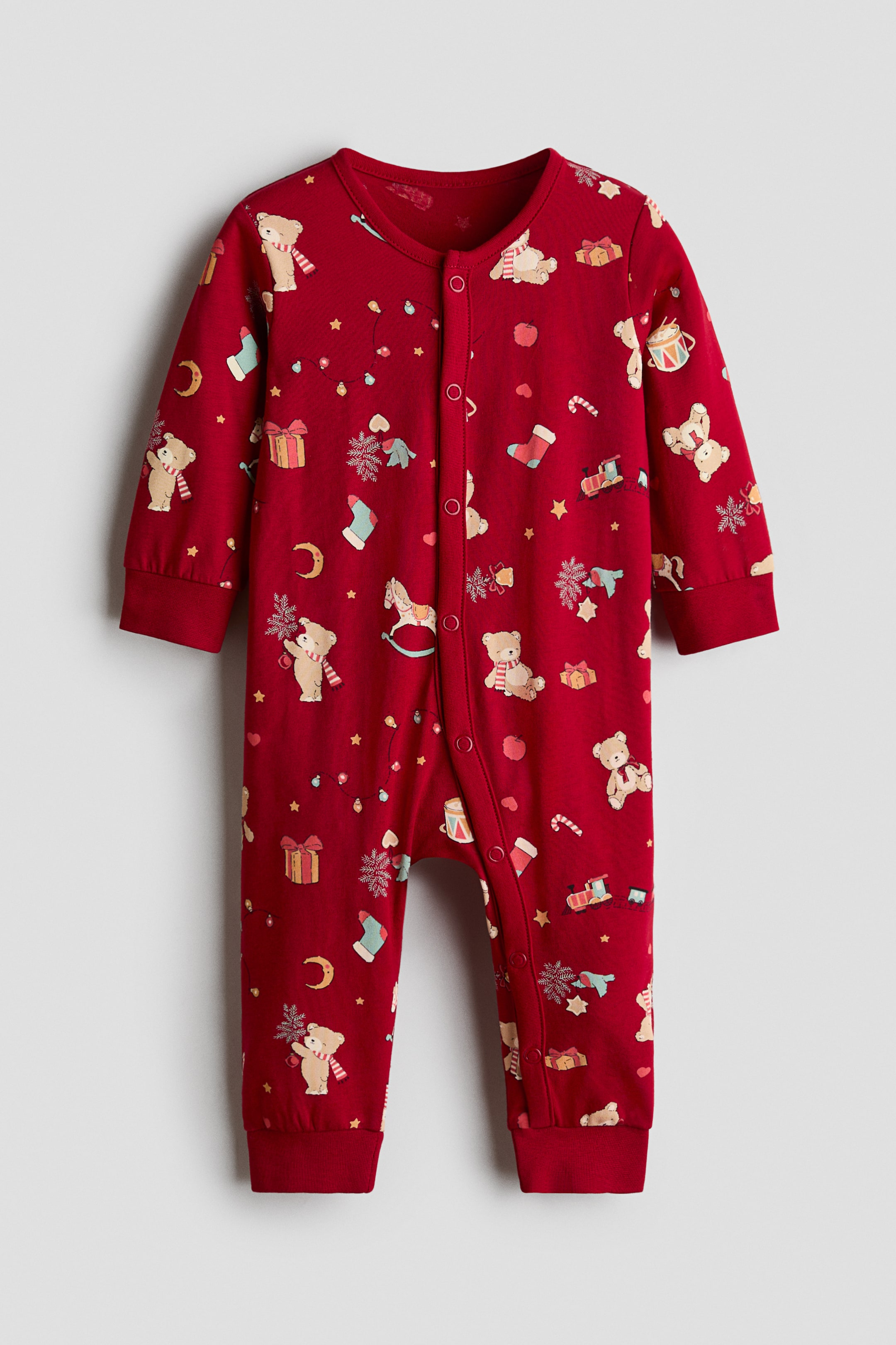 View larger image: A red baby onesie features an allover print of teddy bears, gifts, snowflakes, candy canes, rocking horses, stars, moons, and stockings, with a round neckline, long sleeves with ribbed cuffs, long legs with ribbed cuffs, and snap buttons running from the neckline to the inner thigh.