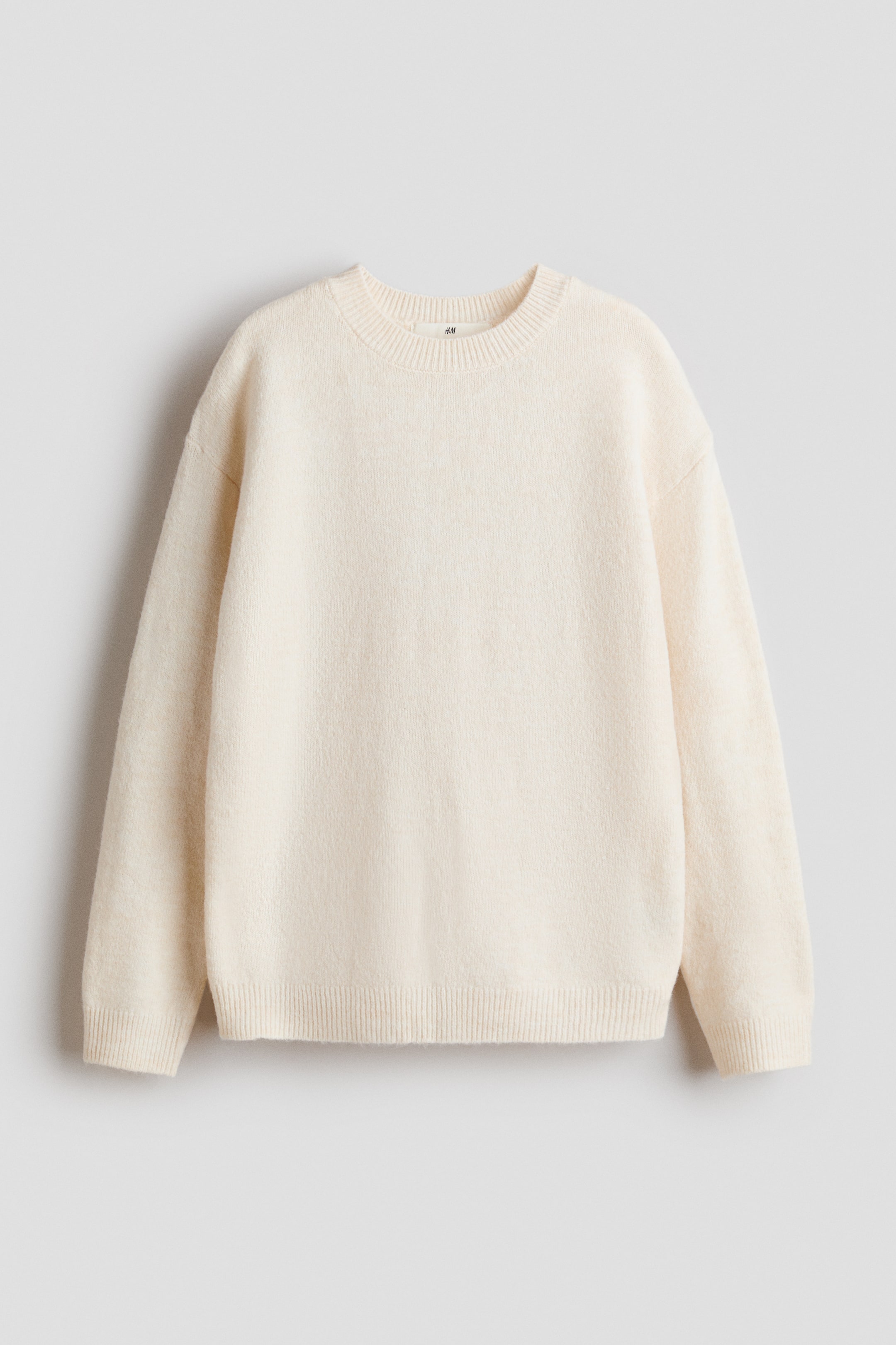 View larger image: A cream-colored sweater is shown from the front, featuring a relaxed fit and a soft knit texture. It is designed with a round, rib-trimmed neckline, dropped shoulders, long sleeves, and ribbed cuffs and hem.