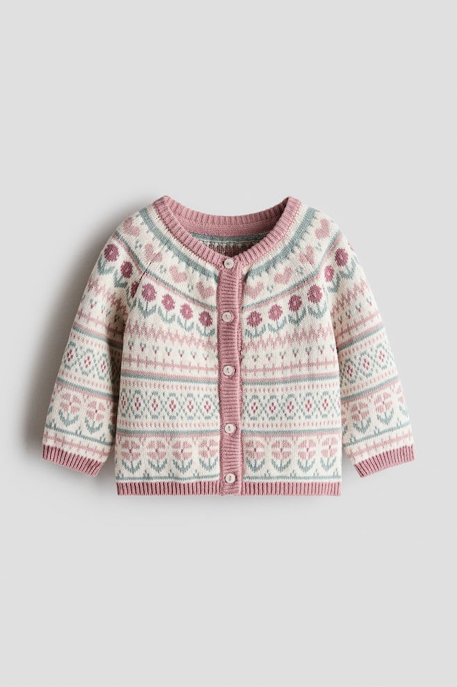This knit cotton cardigan is displaying a cream-colored base decorated with pink flowers, hearts, and green geometric patterns in a front-facing view. The design is featuring long raglan sleeves, a dusty pink ribbed round neckline, placket, cuffs, and hem, with five white buttons securing the front. - 1