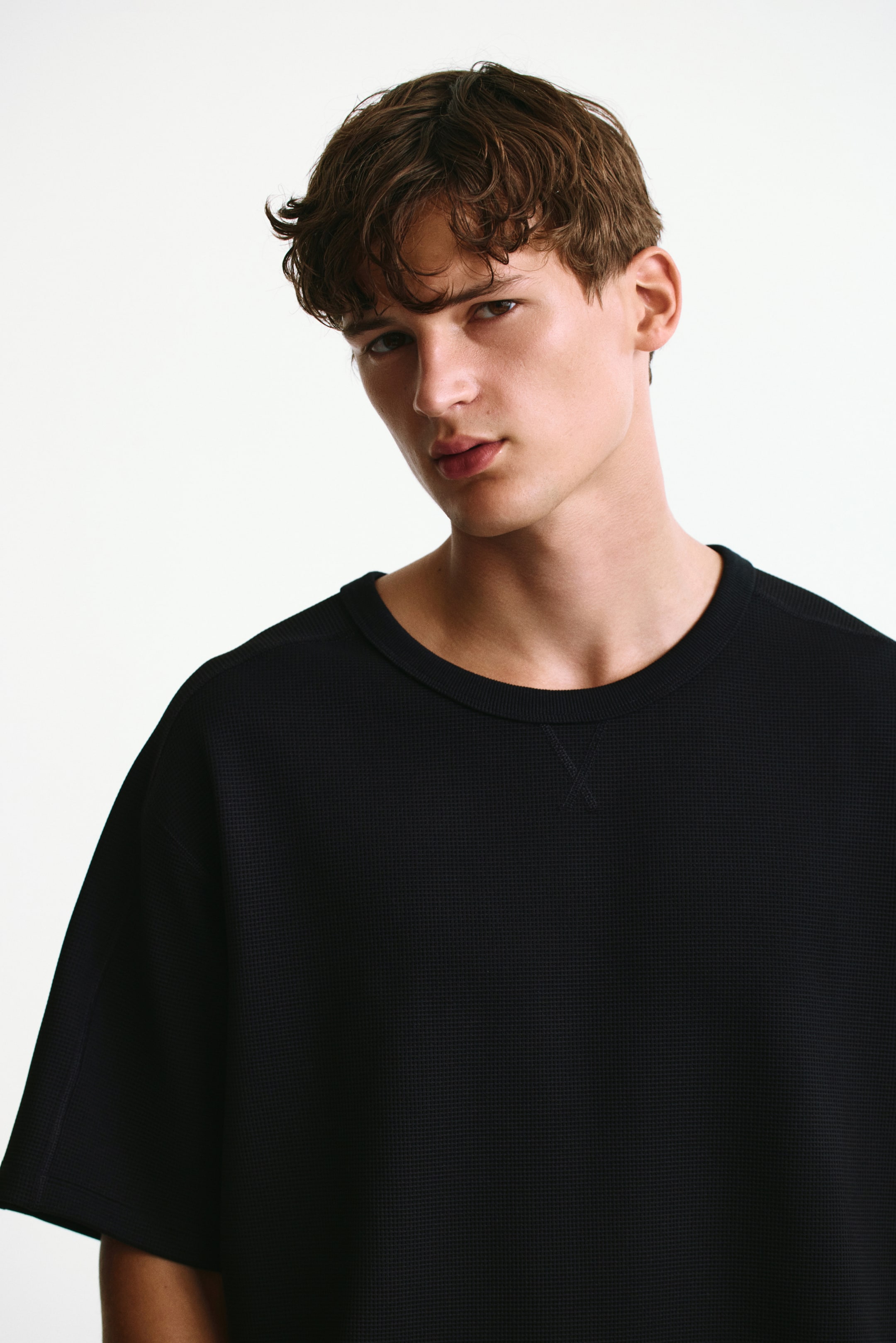 View larger image: A black loose-fit waffled sports T-shirt with DryMove? is being worn by the model. The shirt features a crew neck, short, wide sleeves, and a waffled texture, with a visible V-stitch detail below the neckline.
