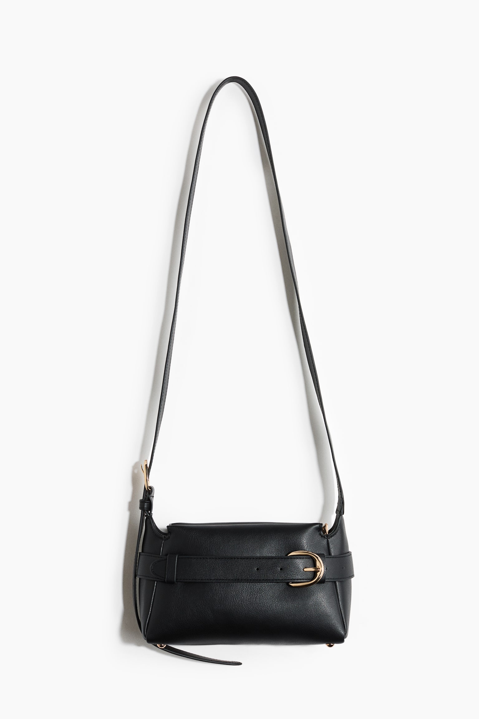 A black crossbody bag is hanging, showcasing its front view. It is made of coated fabric, featuring an adjustable shoulder strap and a zip at the top. A belt-look strap is wrapping around the bag and fastening with a gold-toned metal buckle at the front. - 1