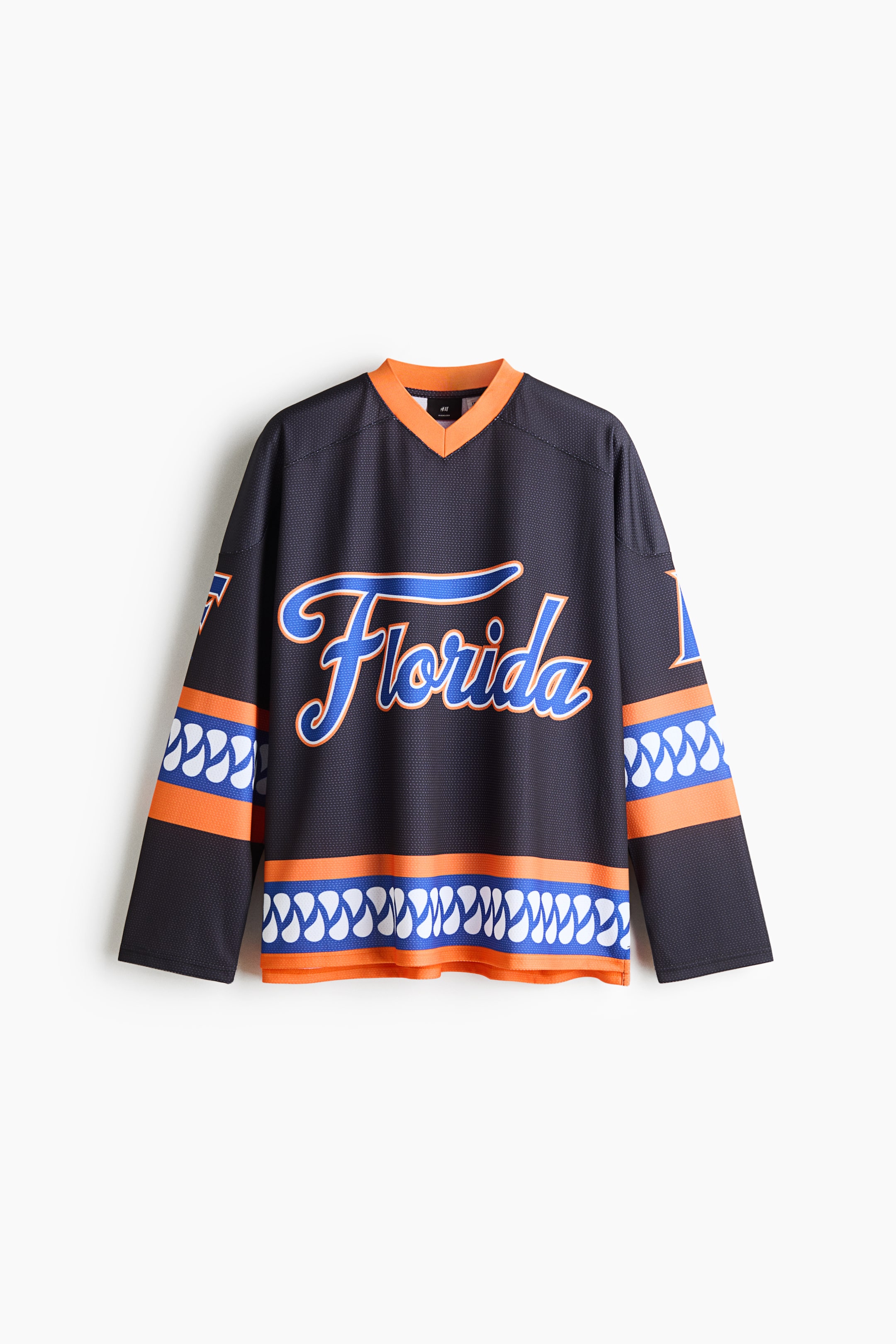View larger image: A front-facing black mesh jersey features a bright orange V-neck collar and a cursive “Florida” graphic in blue and orange across the chest. The long-sleeved garment displays matching striped bands with a white wave pattern along the hem and sleeves.