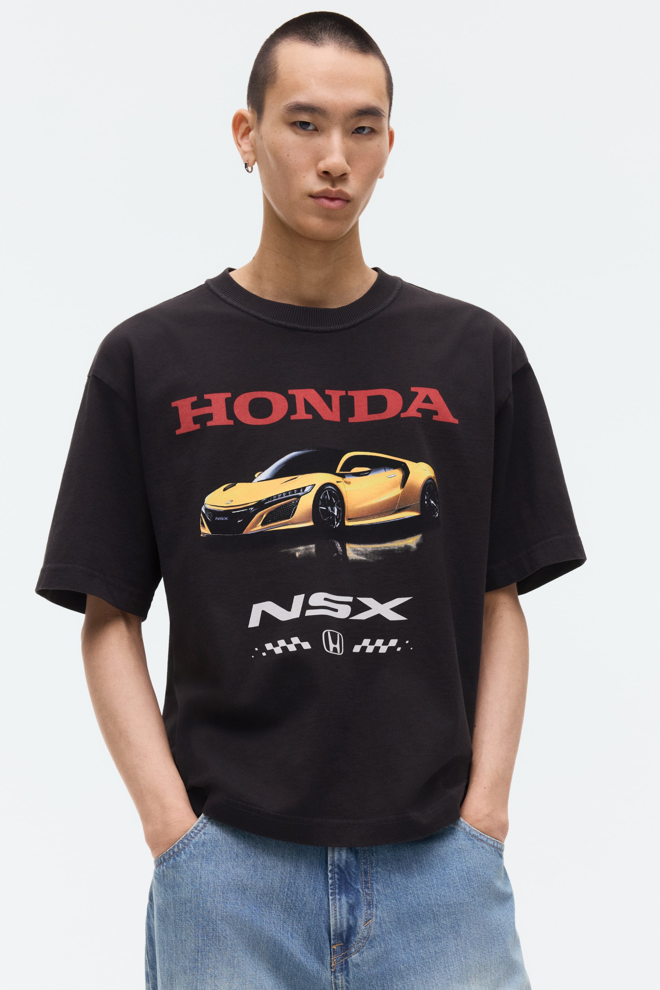 View larger image: A black oversized t-shirt featuring a ribbed crew neck and a large red "HONDA" logo across the chest. Below the logo, a yellow Honda NSX sports car is depicted, angled slightly to the right, with "NSX" text and a checkered flag pattern with the Honda logo shown underneath.