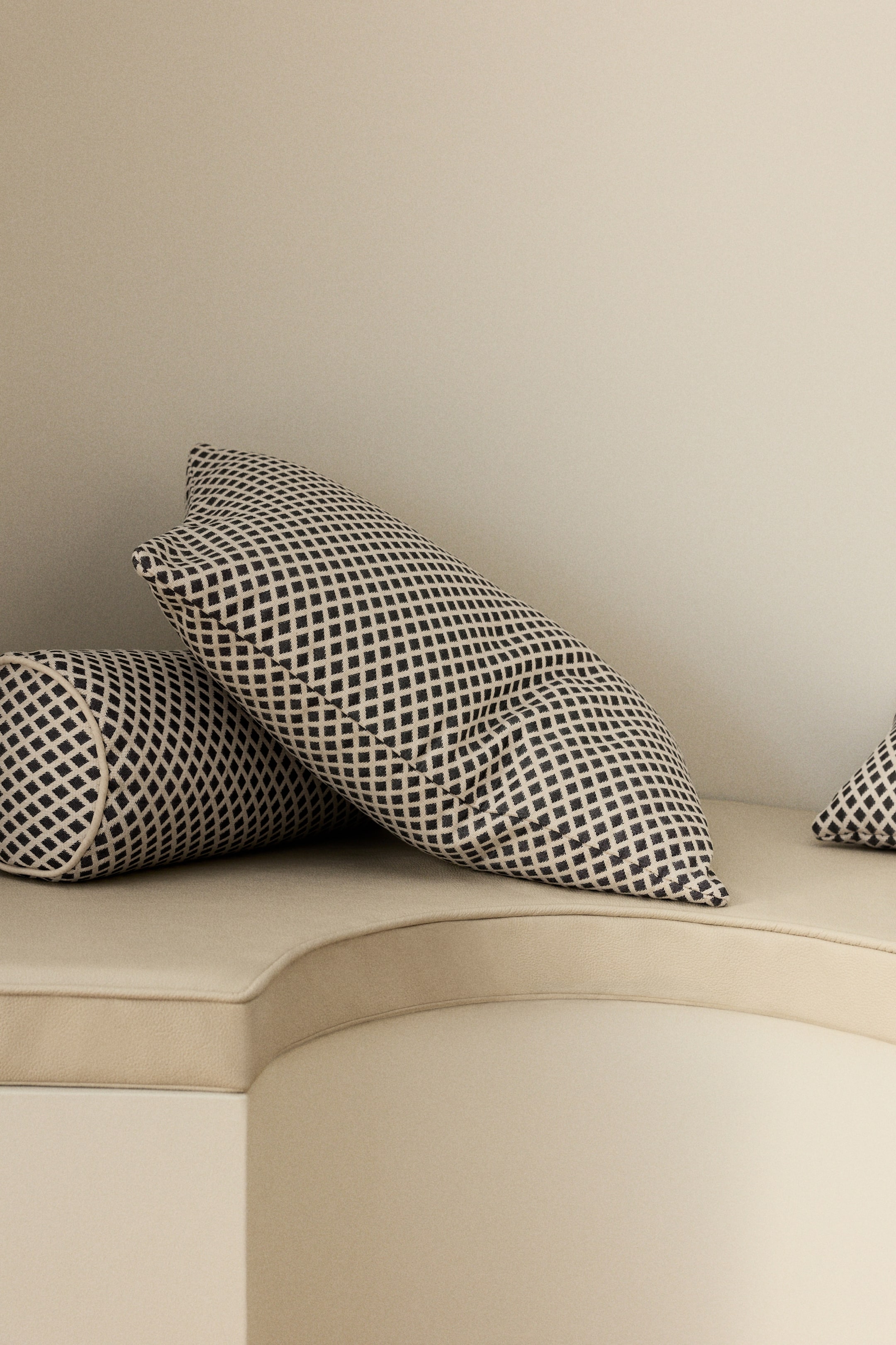 View larger image: Two pillows are set on a light-colored, curved seating surface. One rectangular pillow is positioned forward, showcasing a black and off-white diamond grid pattern. A cylindrical bolster pillow, with the same pattern, lies horizontally behind it.