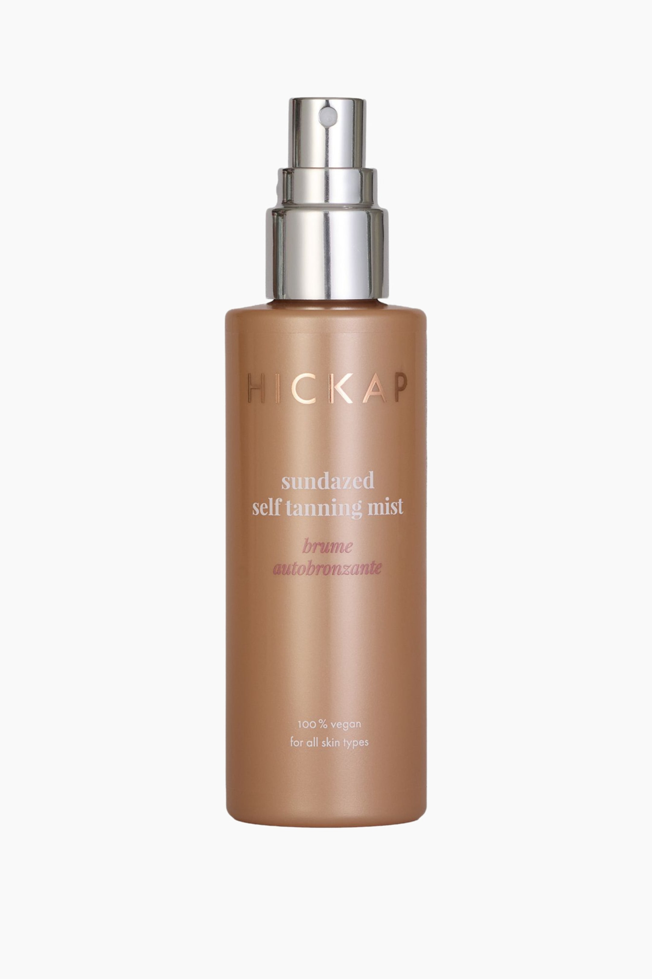 Visa större bild: En bronscylindrisk flaska med brun-utan-sol-spray står upprätt, vänd framåt. Den har en silverfärgad spraypump med ett vitt munstycke, och framsidan visar "HICKAP sundazed self tanning mist" och "brume autobronzante" i ljus text, tillsammans med "100% vegansk för alla hudtyper" längst ner.