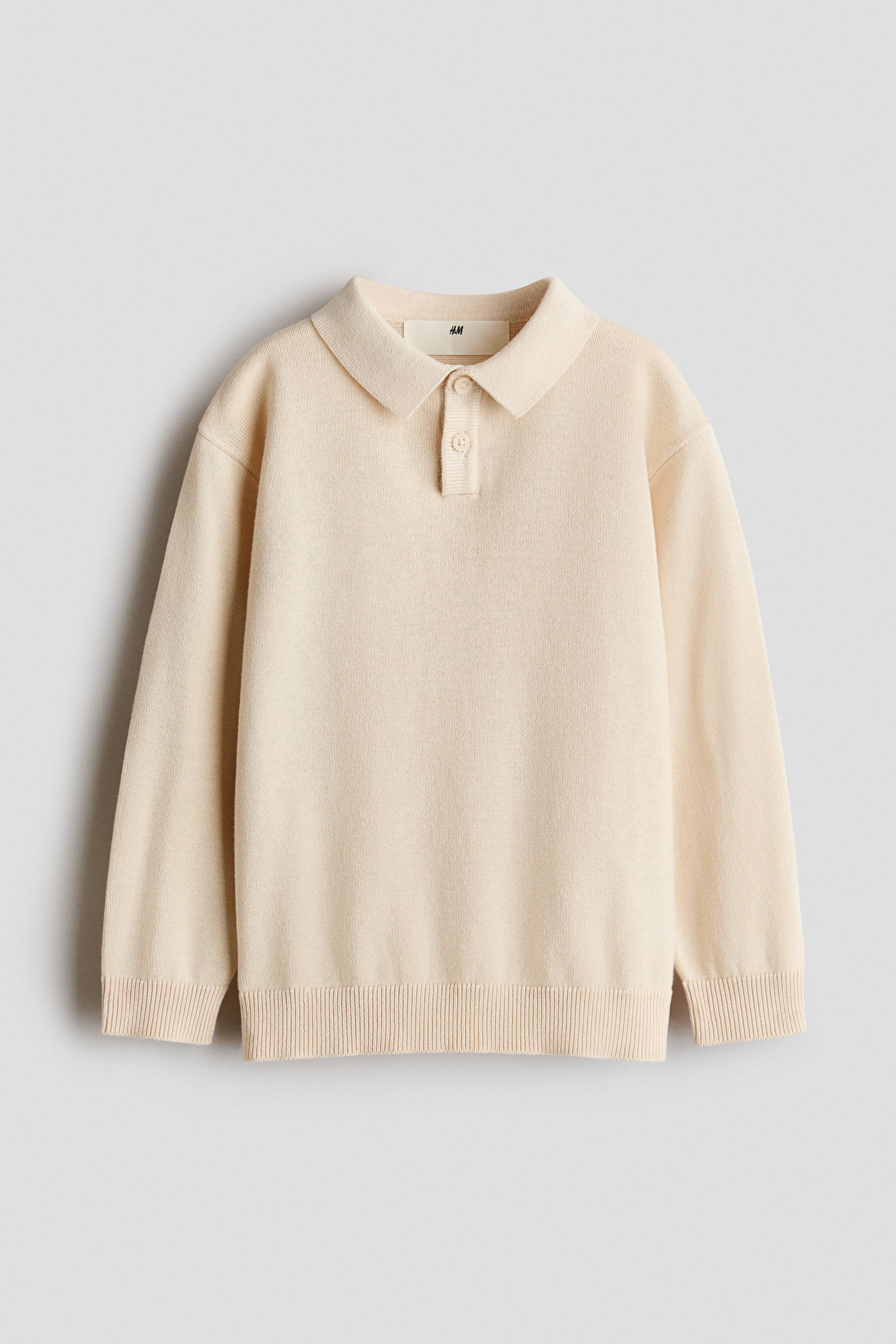 View larger image: A light beige long-sleeved polo jumper is shown from the front, featuring a fine-knit texture, a classic collar, and a two-button placket. Ribbing is visible at the cuffs and hem.