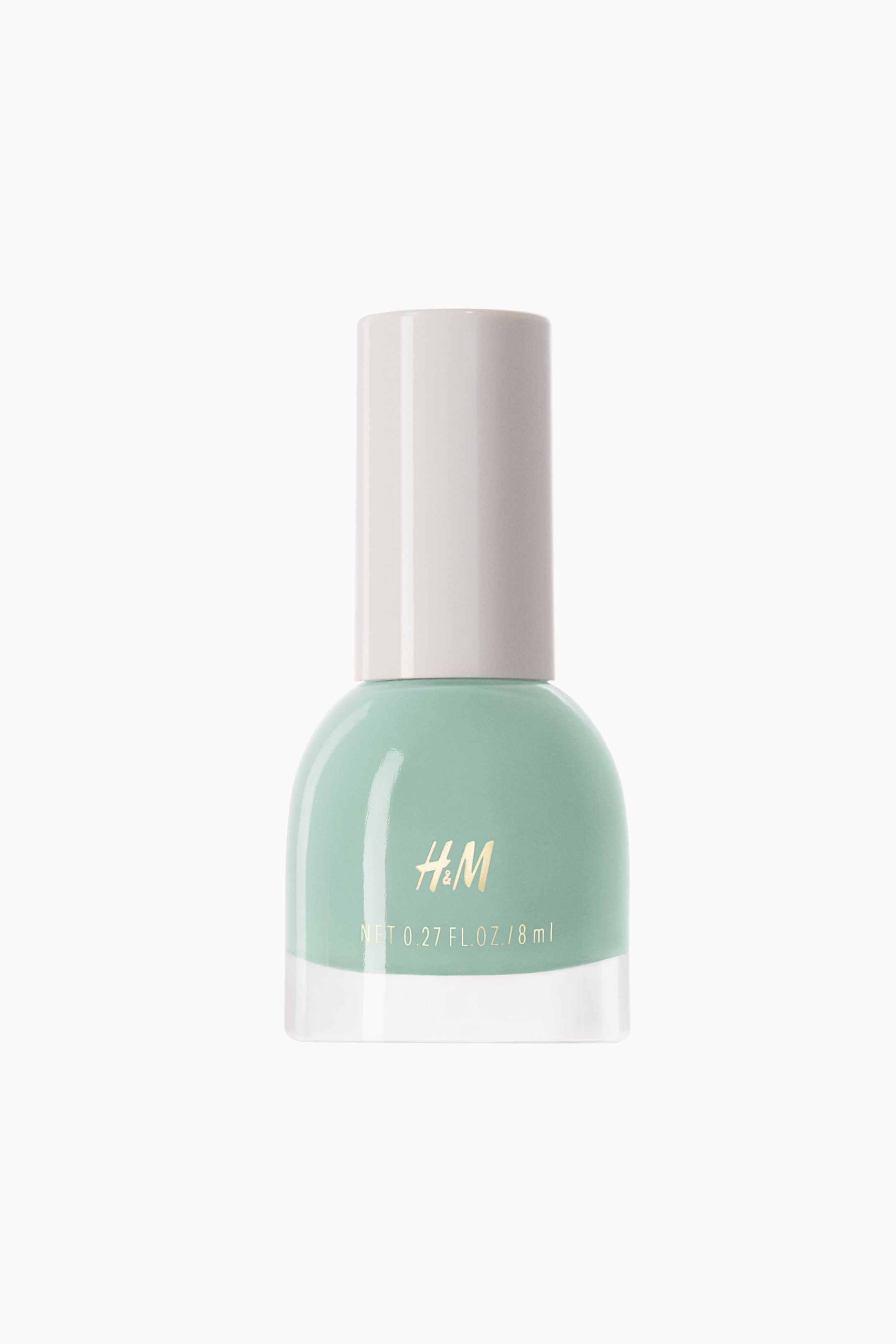 View larger image: Nail polish. The front-facing clear glass bottle contains a mint green polish, featuring a rounded top and a flat base. An opaque light beige cylindrical cap covers the top, with gold 'H&M' branding and volume details visible on the front surface.