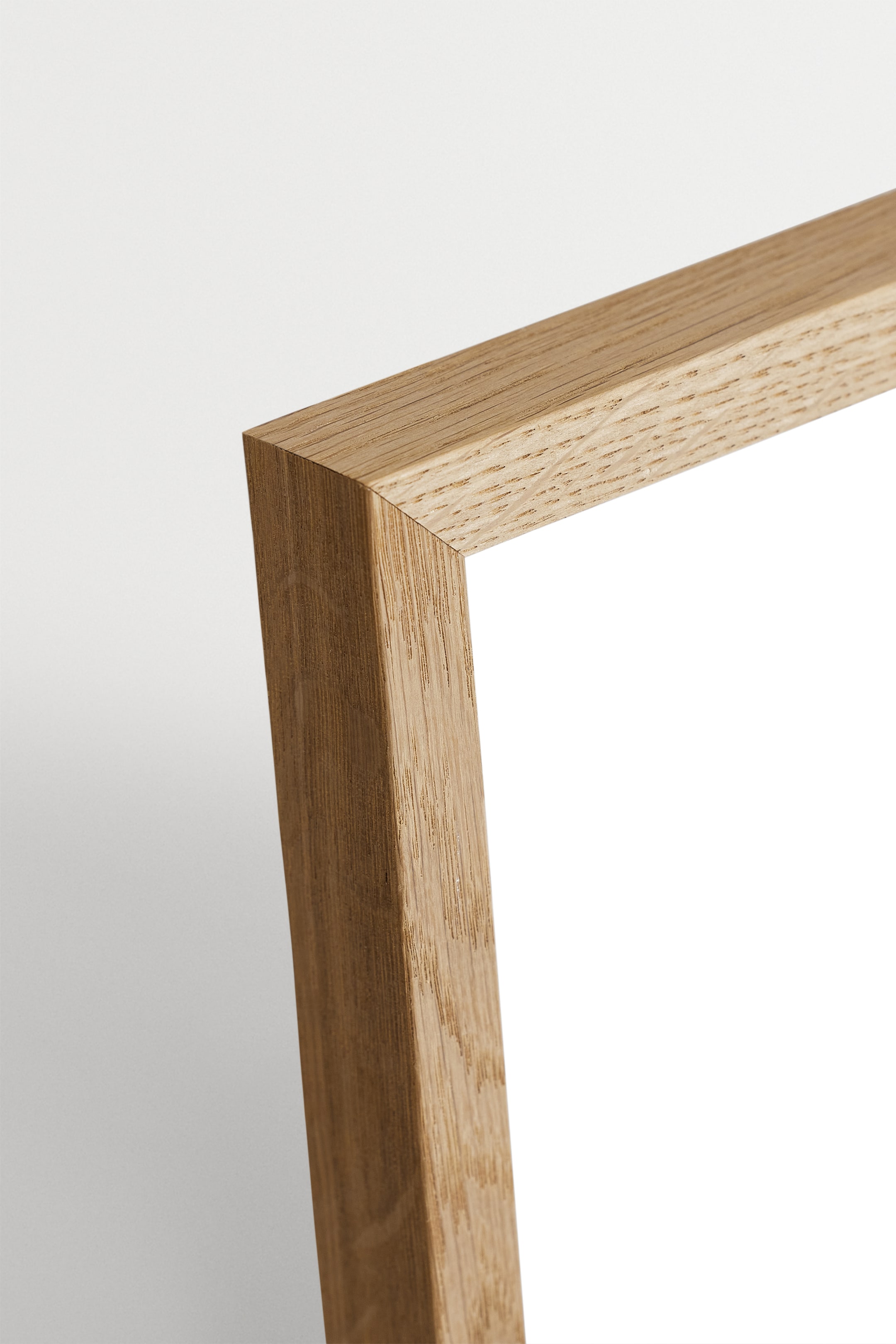 View larger image: A wooden picture frame is angled, presenting its light brown, wood-grained front and side profiles at a mitered corner. It is bordering a clean white inner space.