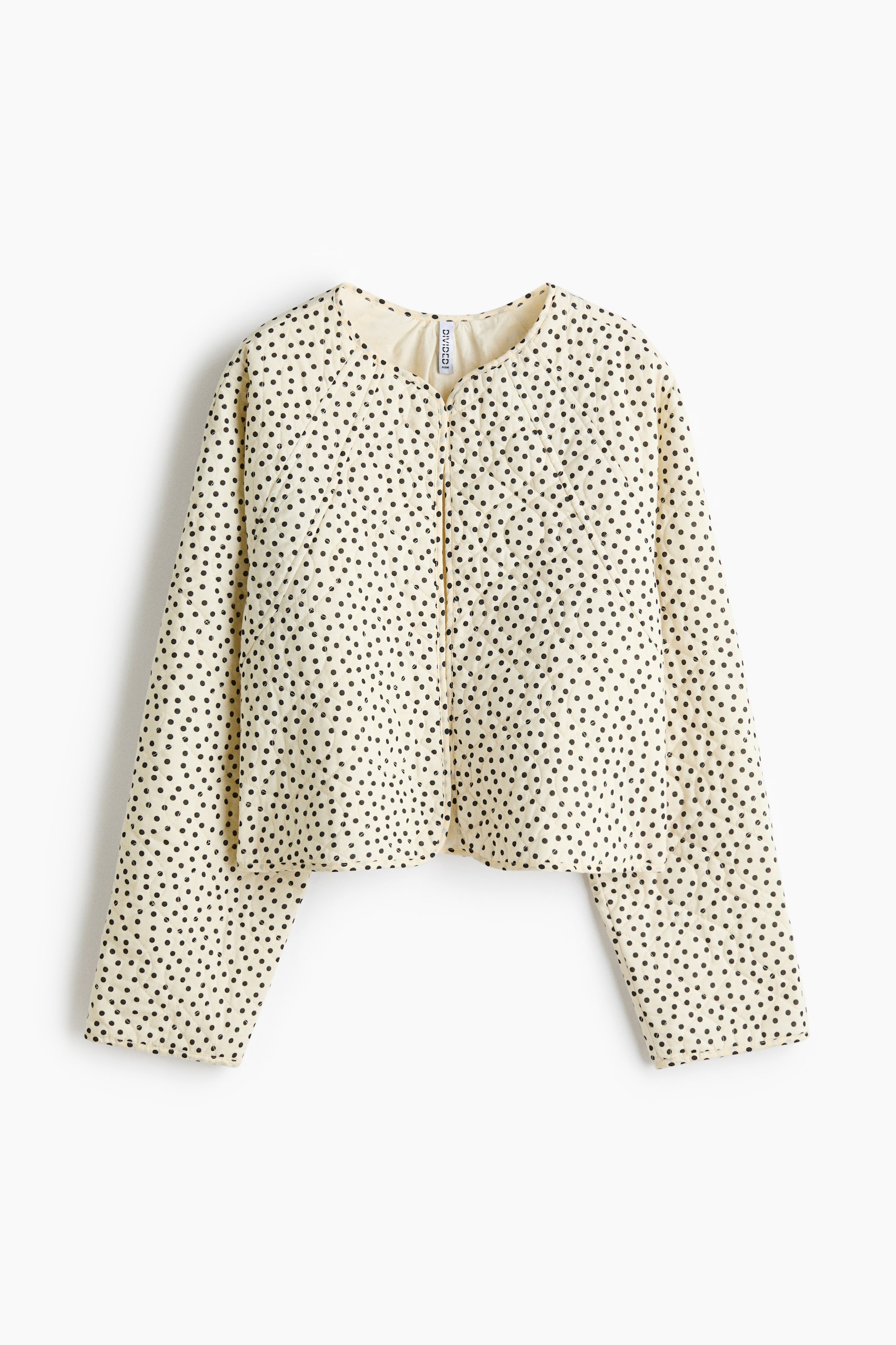 View larger image: A cream-coloured jacket is front-facing, displaying a black polka-dot pattern and a quilted diamond-stitch design. It features a round, collarless neckline and a full-length zip that is slightly open at the top, along with long, wide sleeves and a cropped hem.