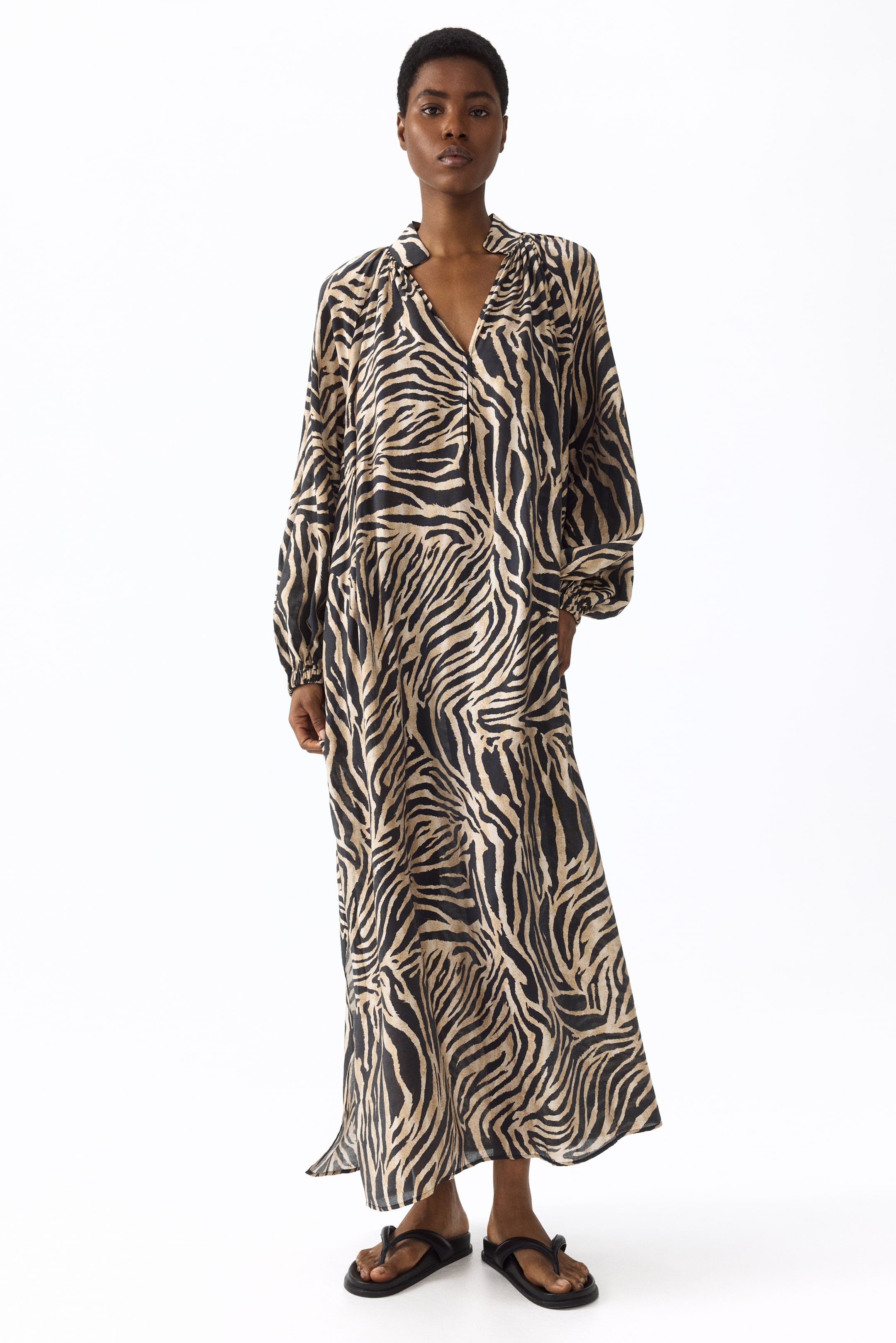 Zobraziť väčší obrázok: Maxi šaty sú ozdobené čierno-hnedým zebrovým vzorom a majú výstrih do V so stojacím golierom a nariasením pri výstrihu. Sú navrhnuté s dlhými balónovými rukávmi s nariasenými manžetami a majú voľnú, plynulú siluetu.