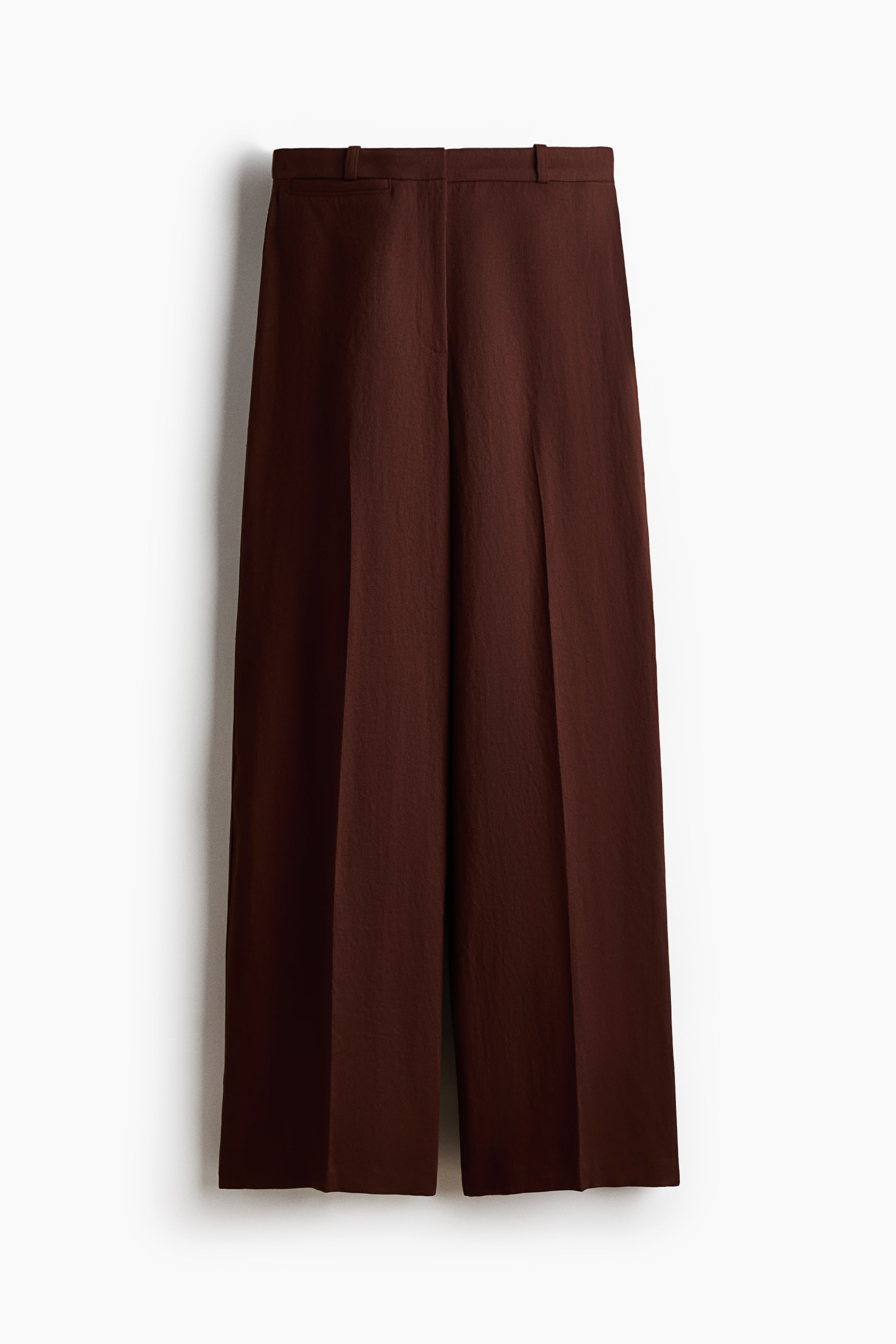 View larger image: Brown tailored trousers are facing FRONT. They showcase a soft twill fabric, a high waist with a zip fly, a faux welt pocket detail on the right side, and wide legs with sharp creases down the front.