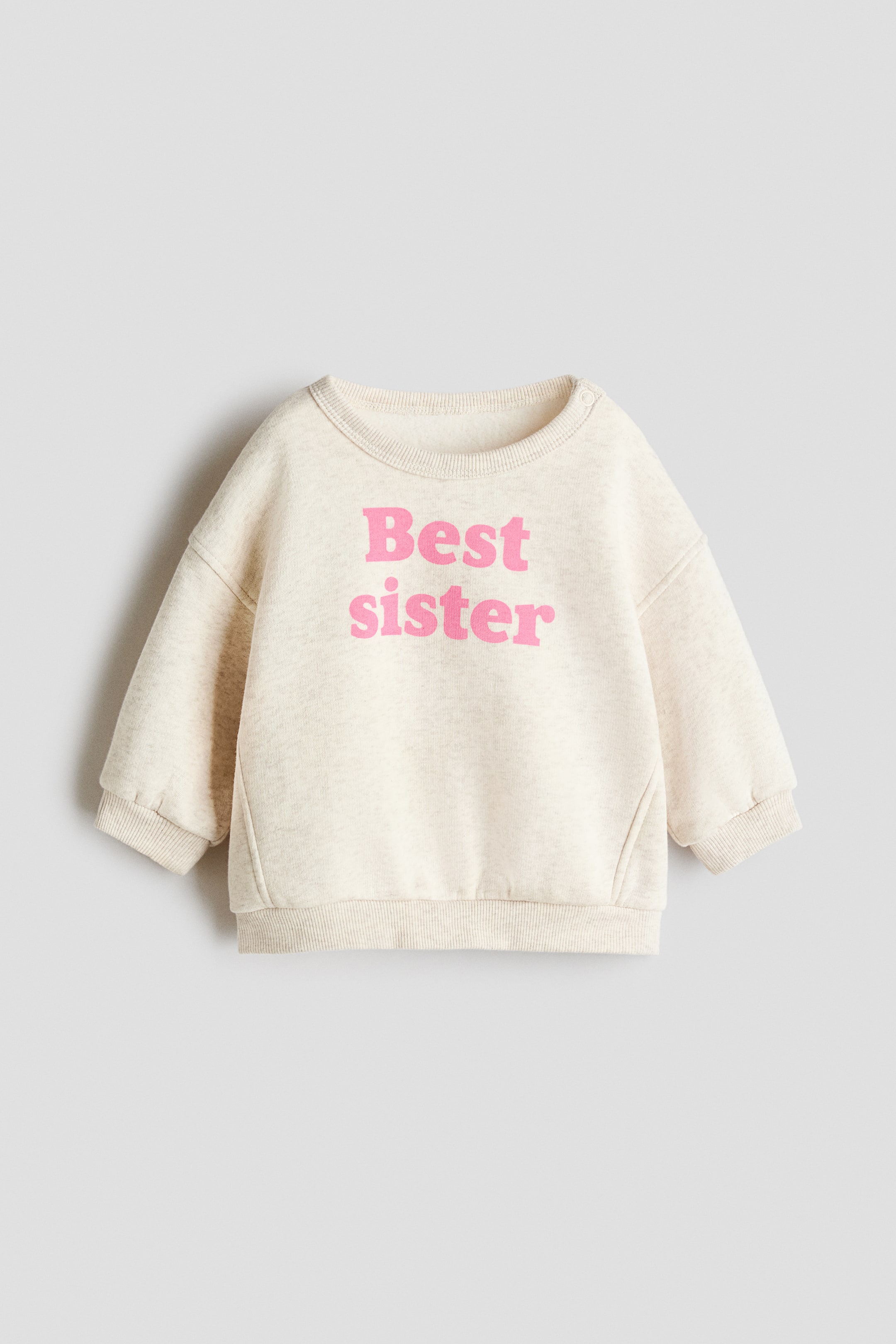 View larger image: A cream flecked sweatshirt is presented FRONT, featuring a pink "Best sister" graphic across the chest. It is designed with a ribbed crew neck, a snap button closure on the left shoulder, and ribbed cuffs and hem.