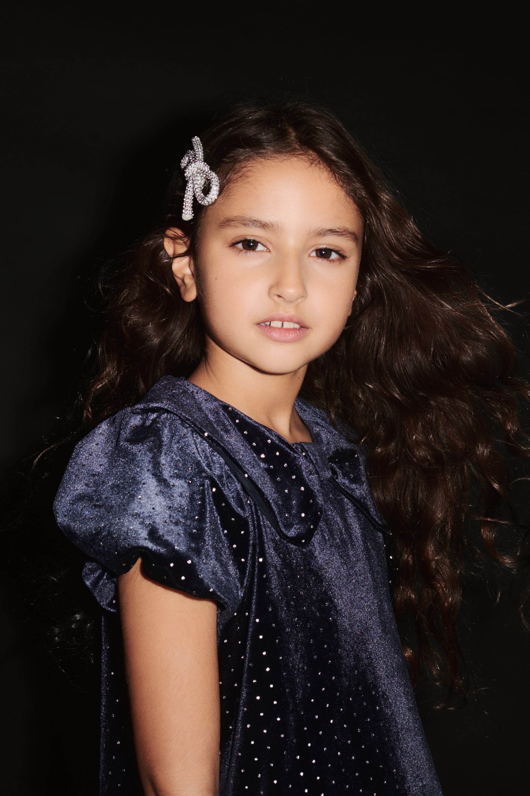 View larger image: A dark blue velvet dress featuring sparkling rhinestone embellishments, short puff sleeves, and a large collar, shown from a three-quarter angle facing left.