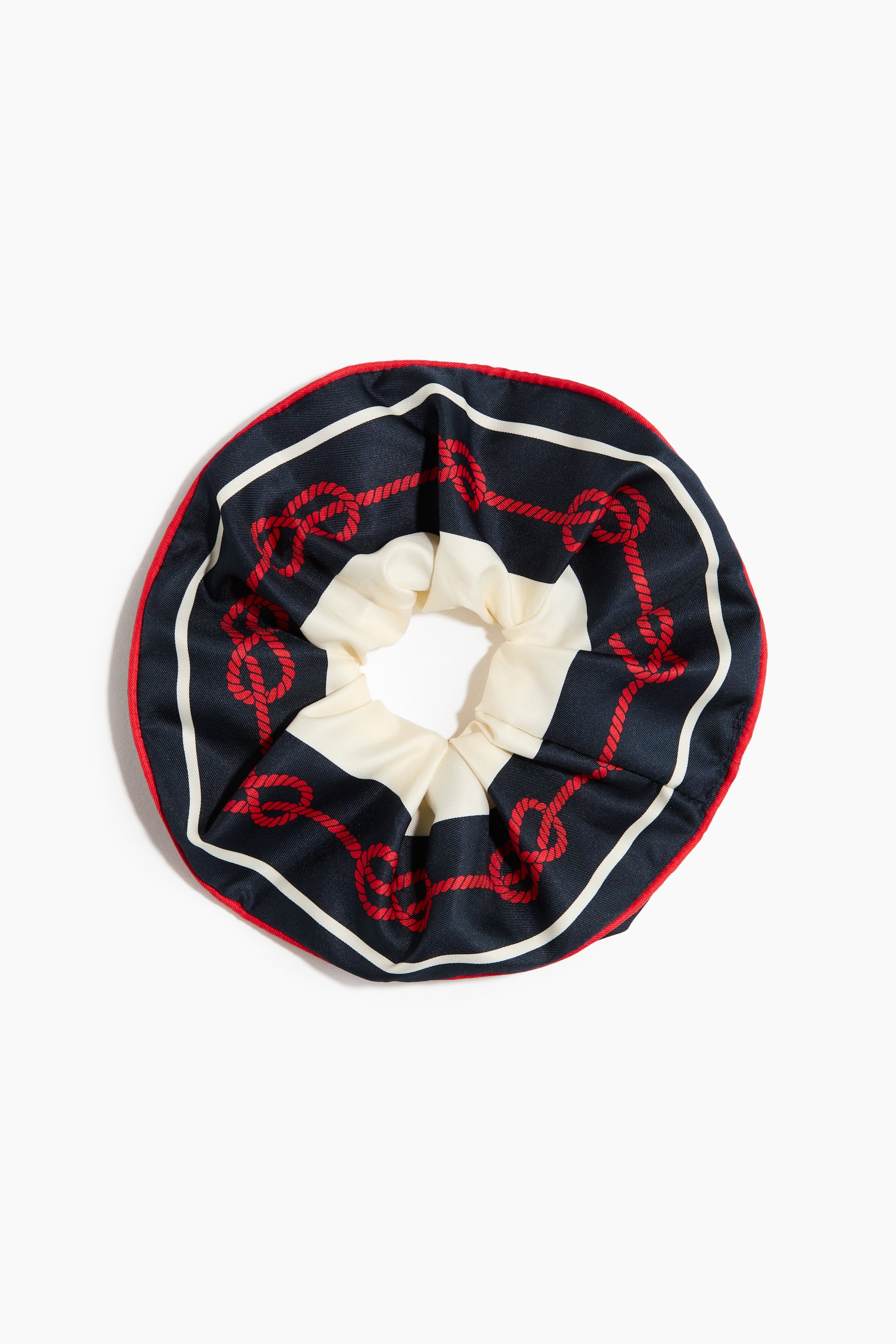 Visualizza immagine più grande: Un scrunchie mostra un motivo a tema nautico su tessuto blu navy e color crema, ripreso frontalmente. Presenta disegni di corde rosse e righe bianche, con bordo esterno rosso.