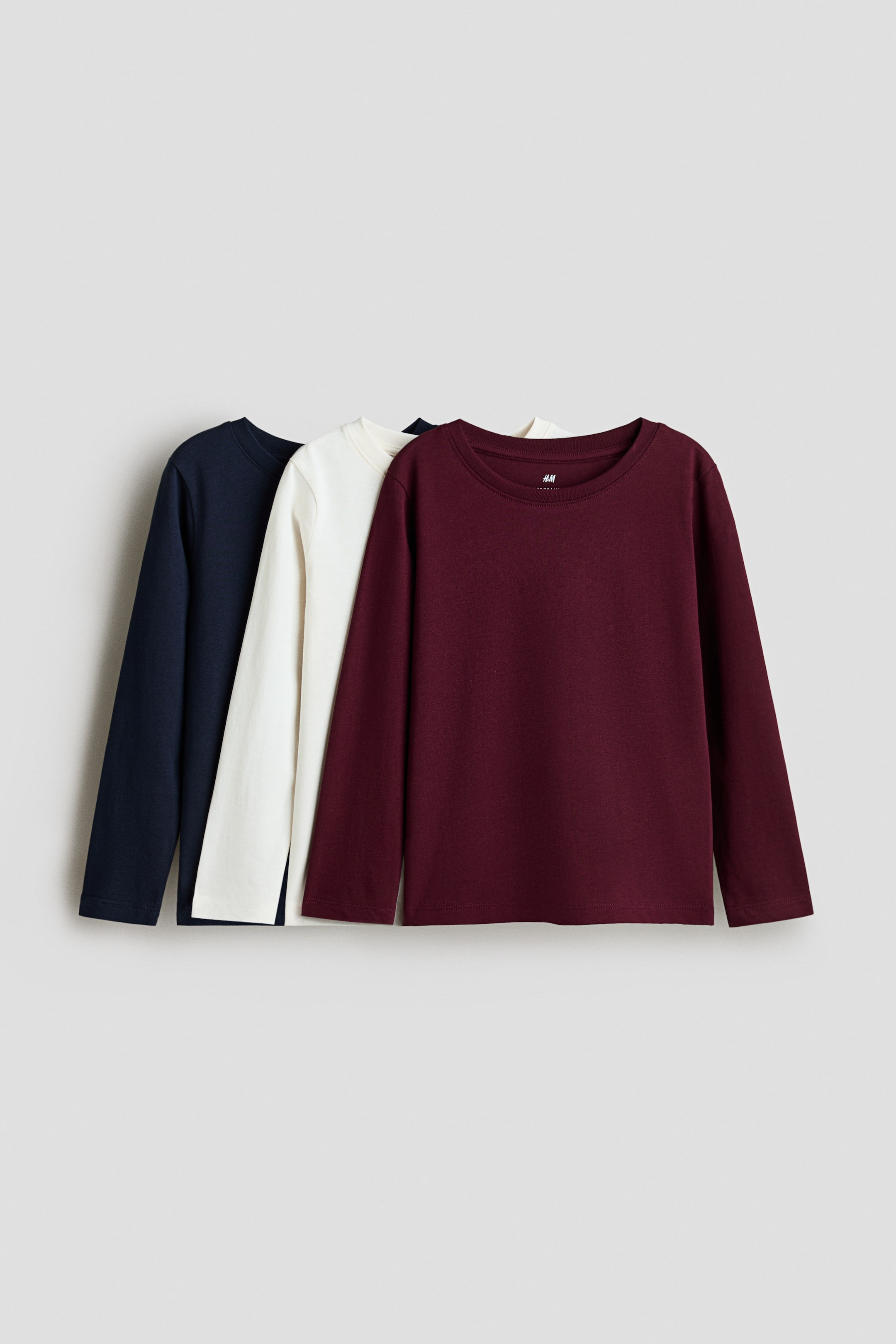 View larger image: Three long-sleeved tops crafted from soft cotton jersey are showcased from the front, each boasting a round neckline with a narrow trim and long sleeves, available in dark blue, off-white, and maroon hues.