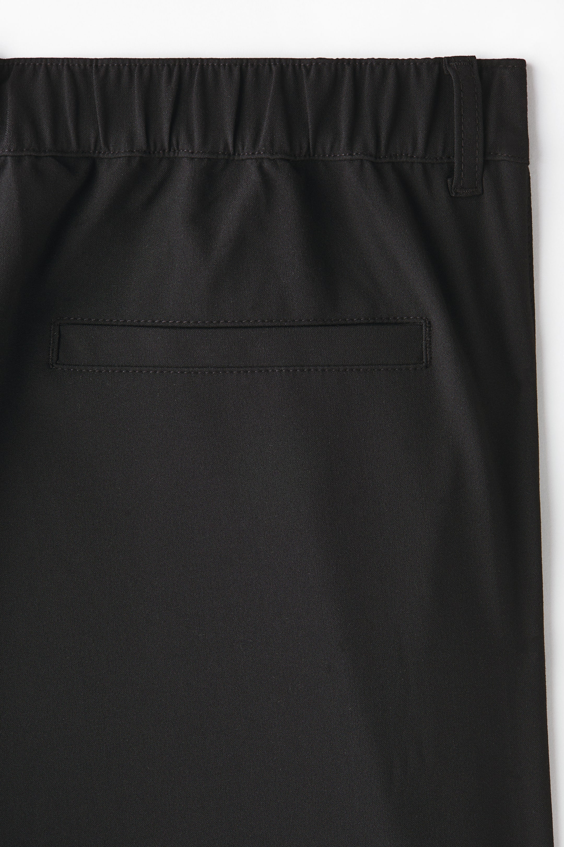 Xem ảnh lớn hơn: Quần tây đen có phần cạp co giãn, nhún với các vòng đai thắt lưng nổi và một túi ngang có viền nằm phía dưới.